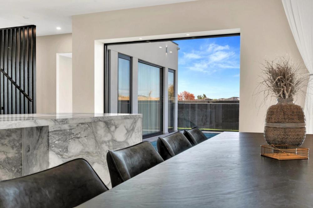 Dining table beside a marble waterfall island with doors to the yard, Tiffany Walk Residence, Sanctuary Lakes