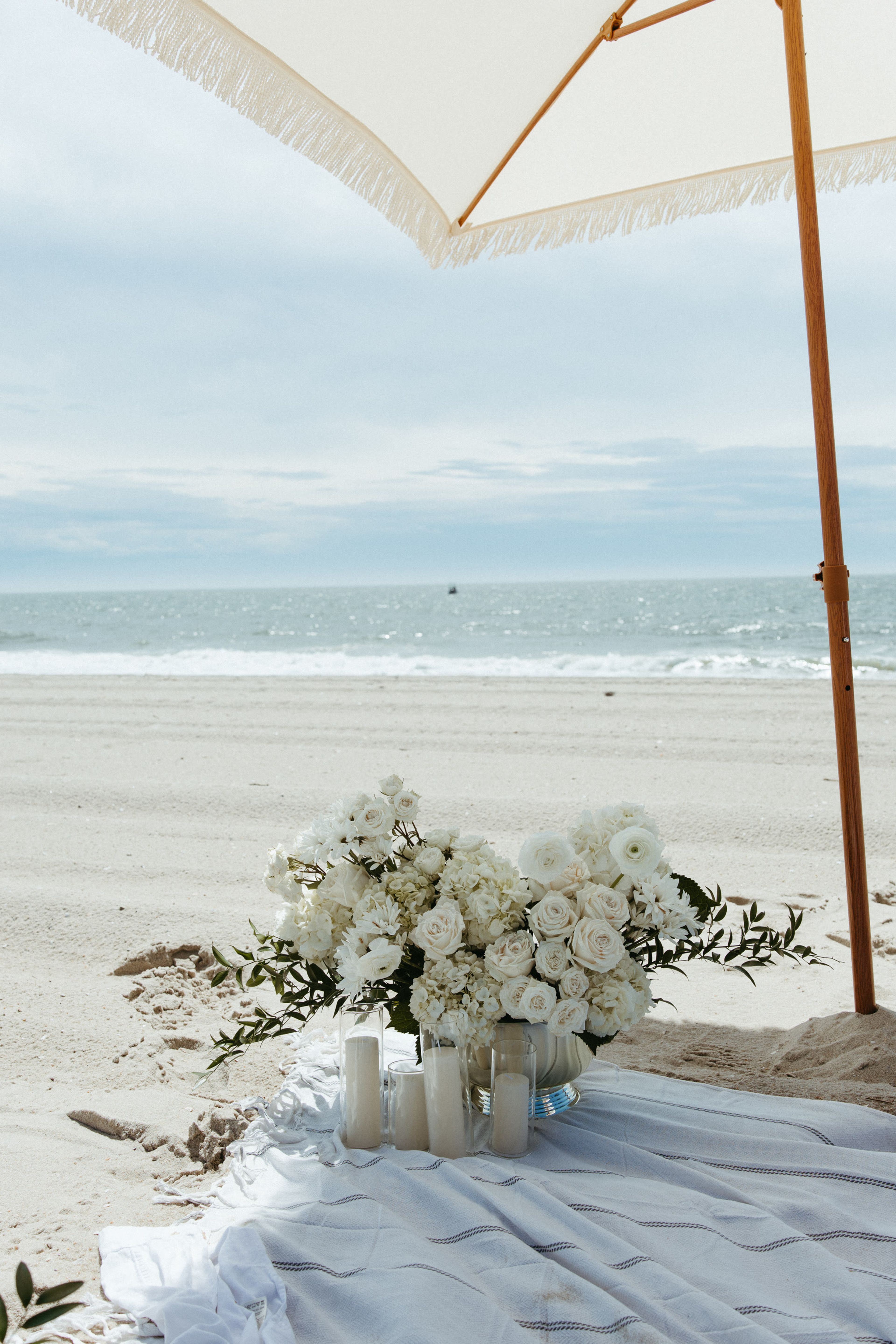 White florals arranged on the sand under a clouded sky
