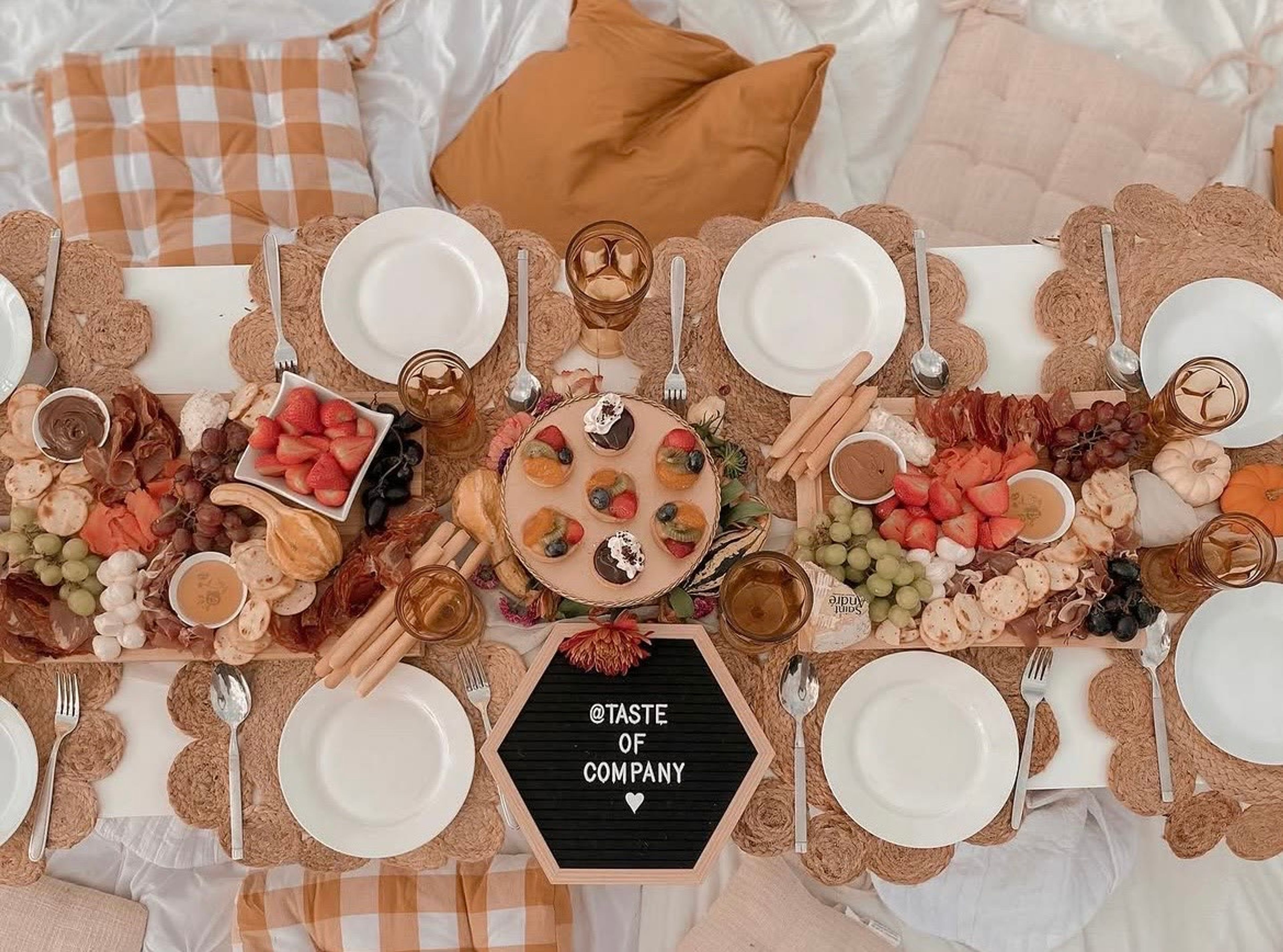 A gingham picnic table laid with plates and a round grazing board