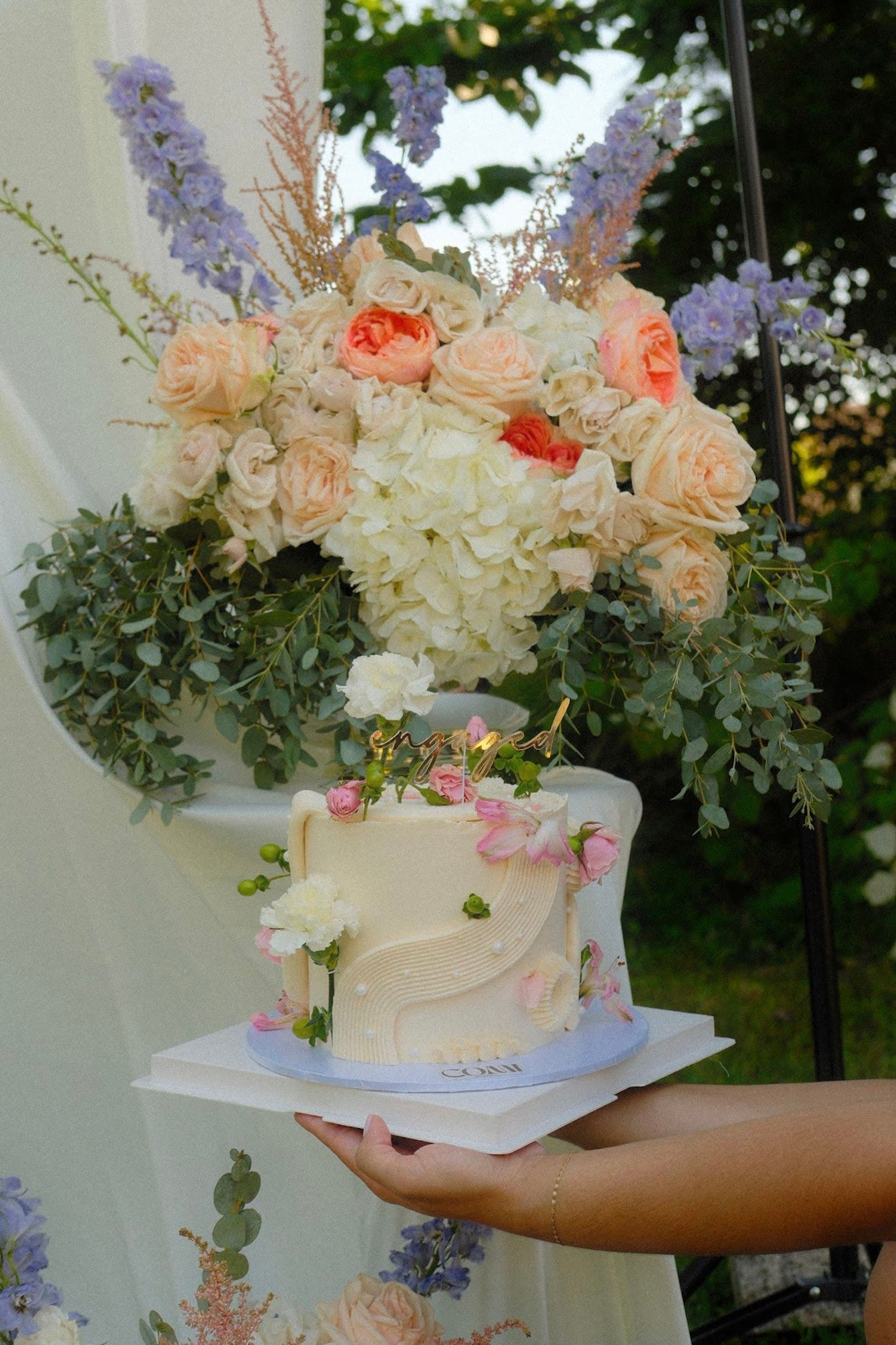 A tiered cake held up in front of the floral backdrop