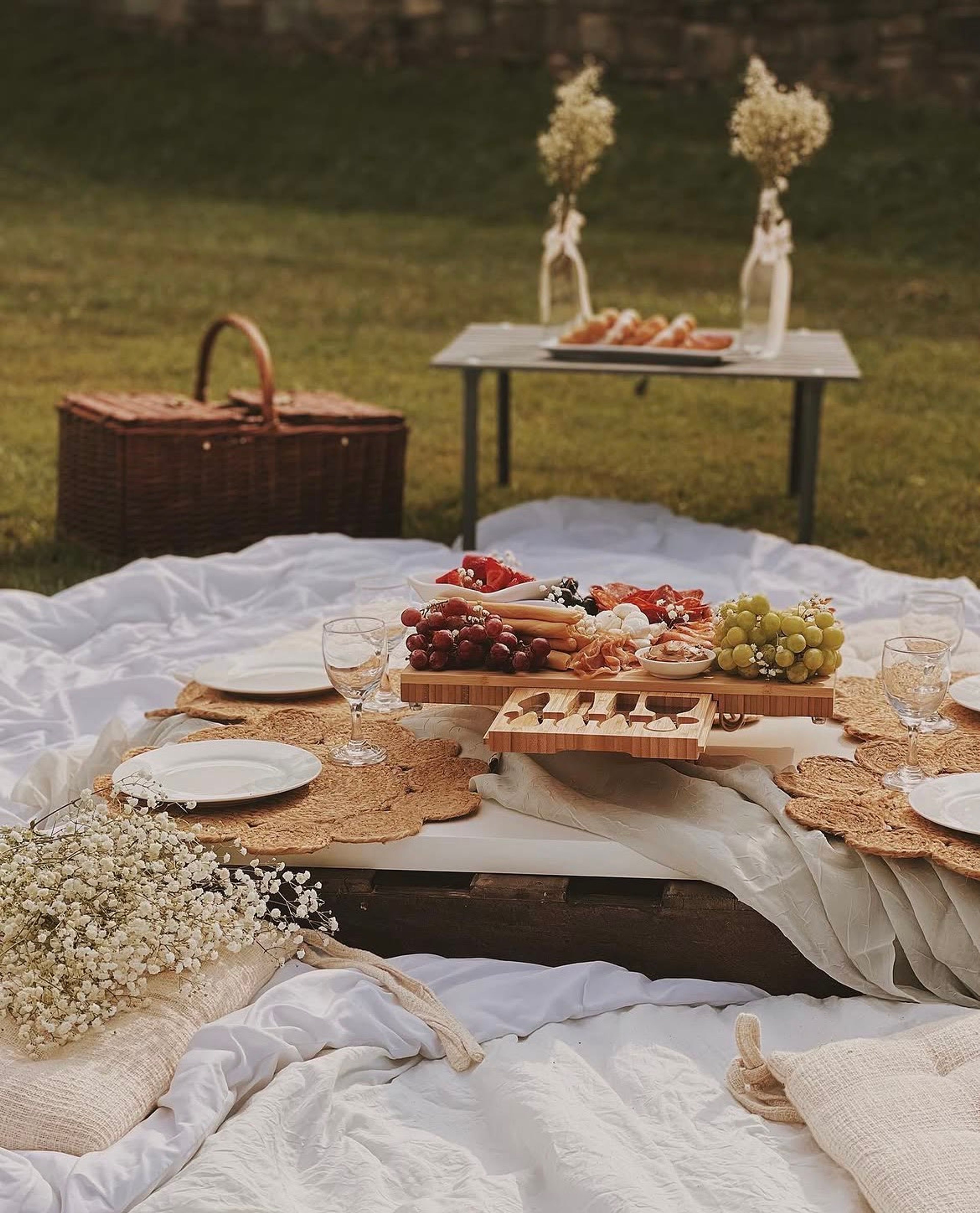 A picnic blanket set with a grazing board and a wicker basket