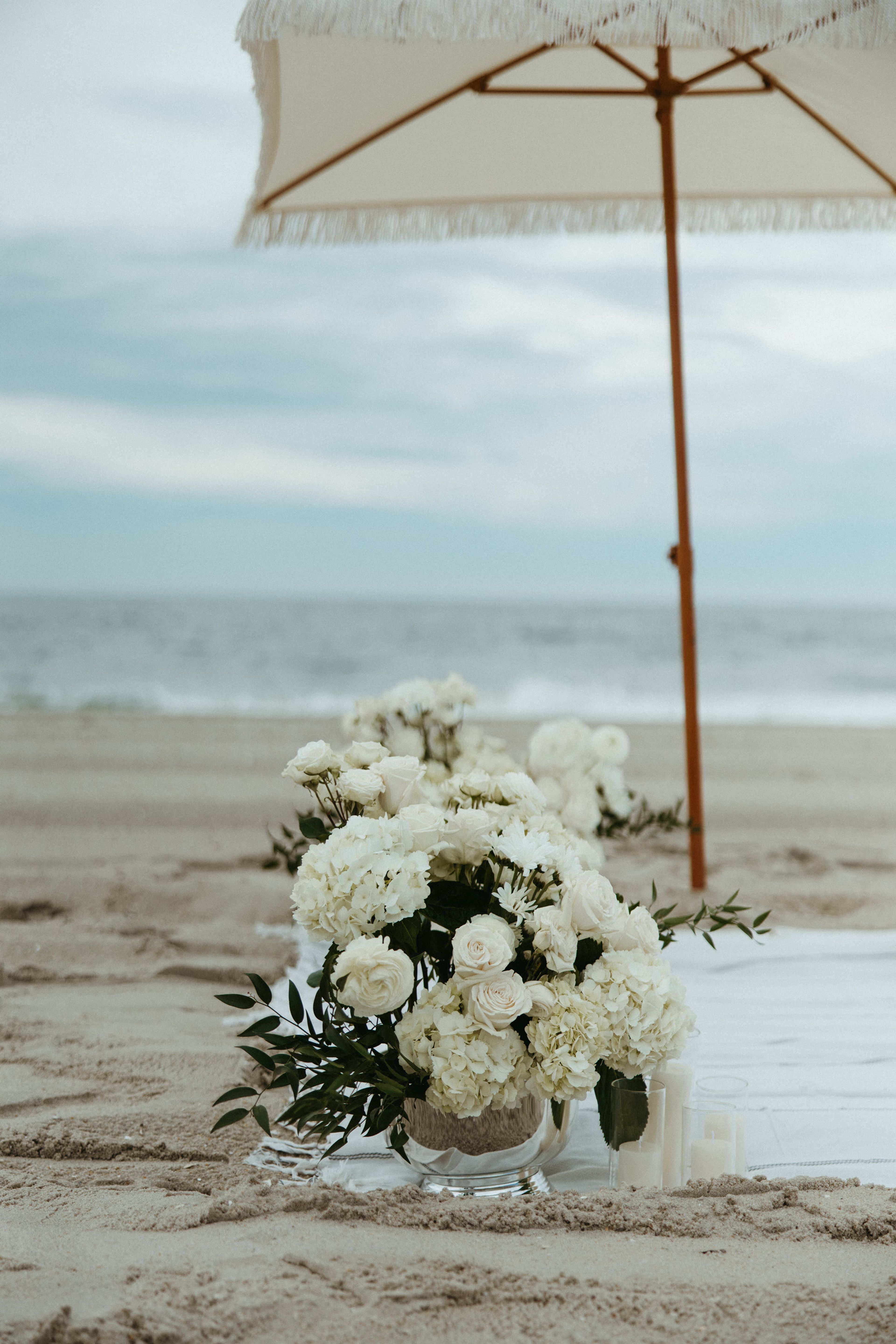 White hydrangea and roses on the sand beside a parasol