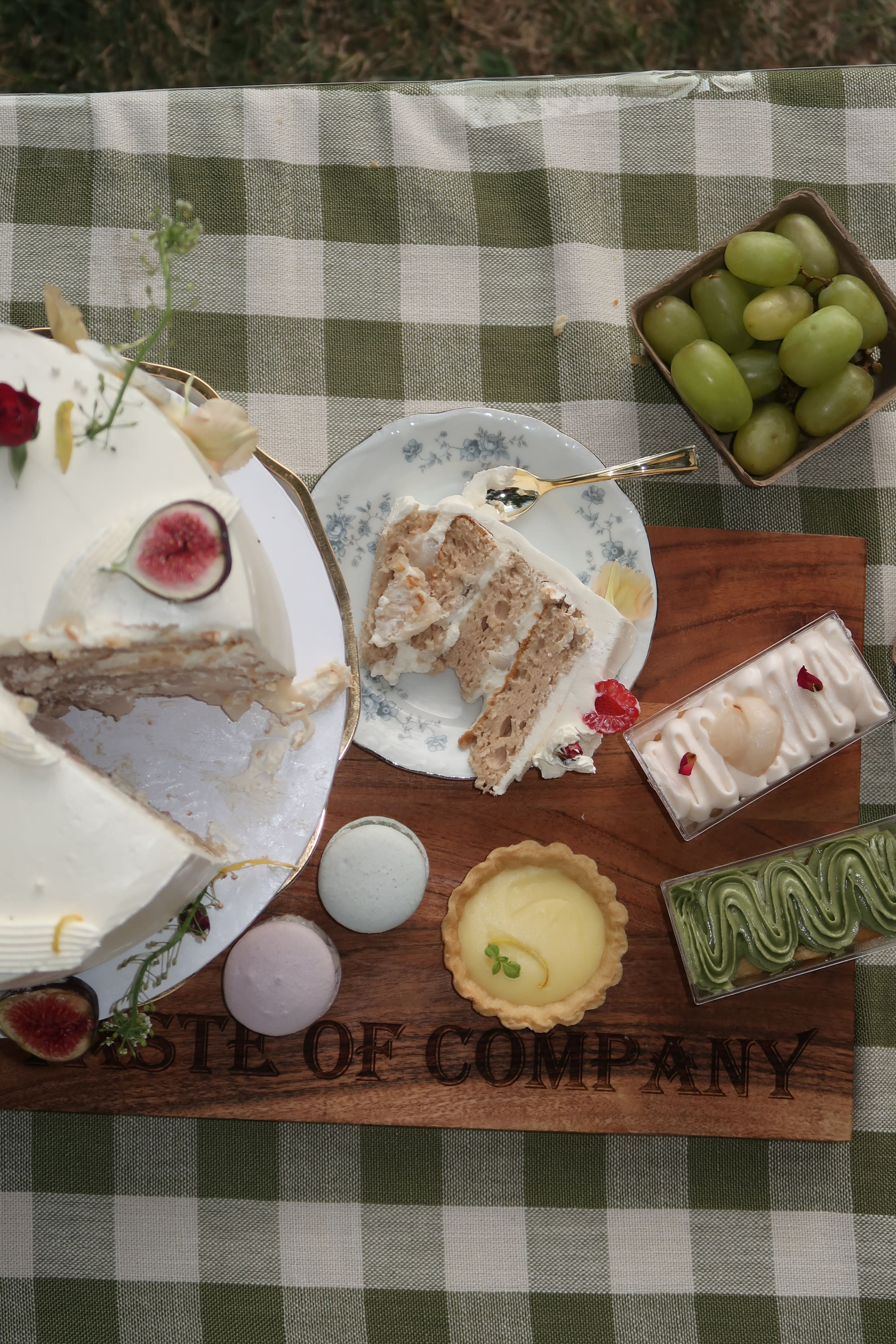 A sliced layer cake on a wooden board with tarts and fruit