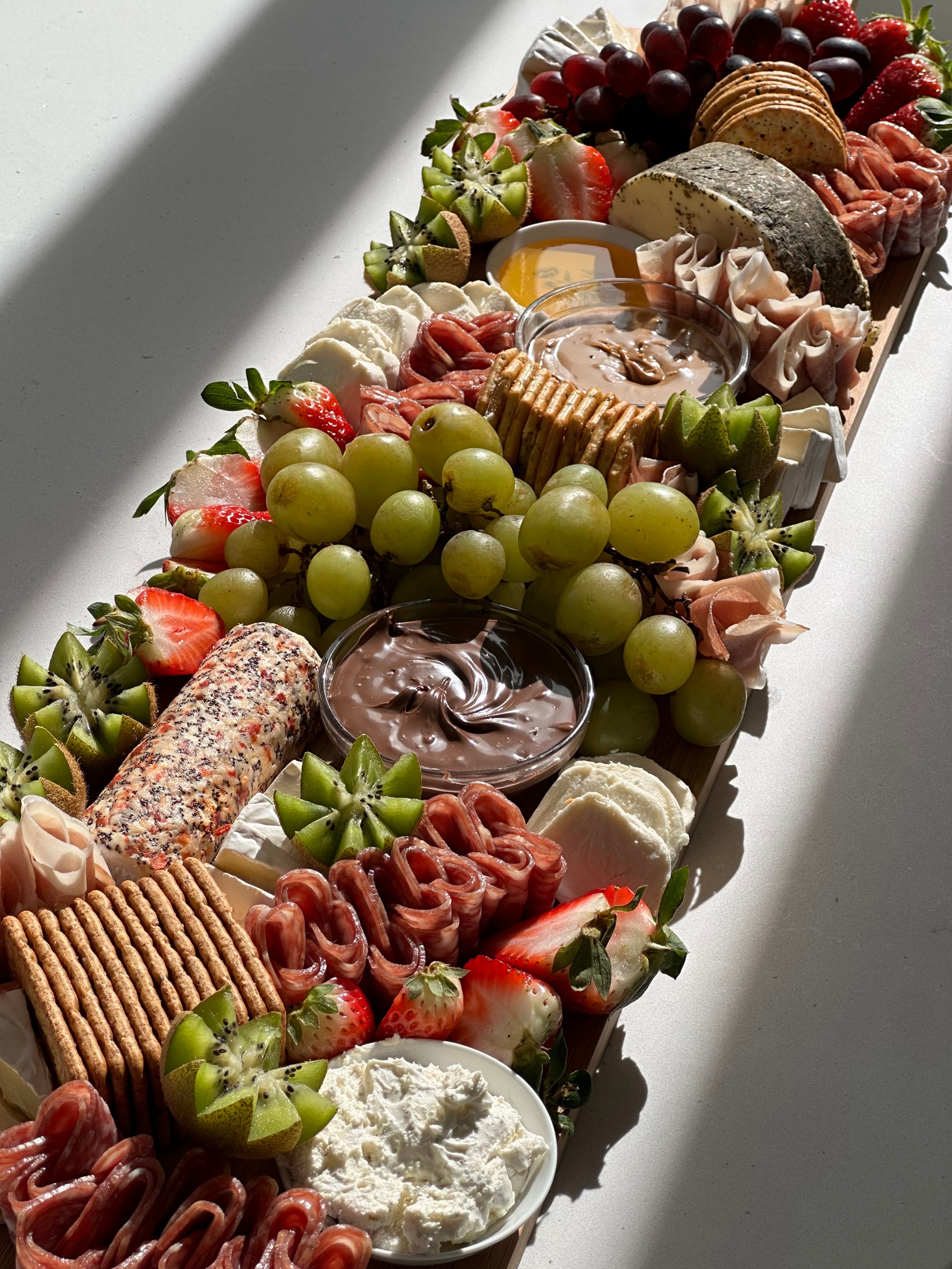 A board of grapes, chocolate dip and pretzels in window light