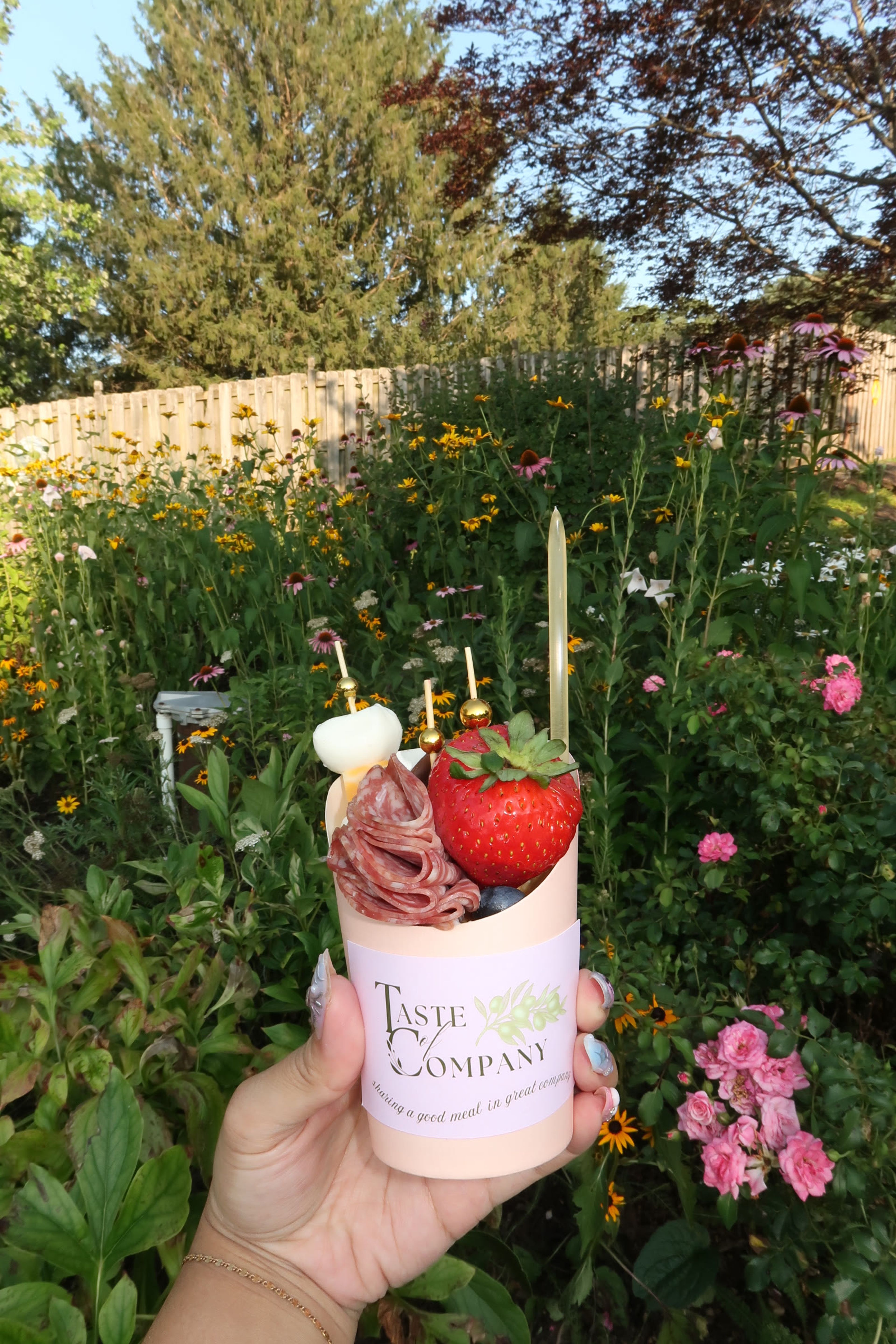 A charcuterie cup with a strawberry skewer, held in a flower garden