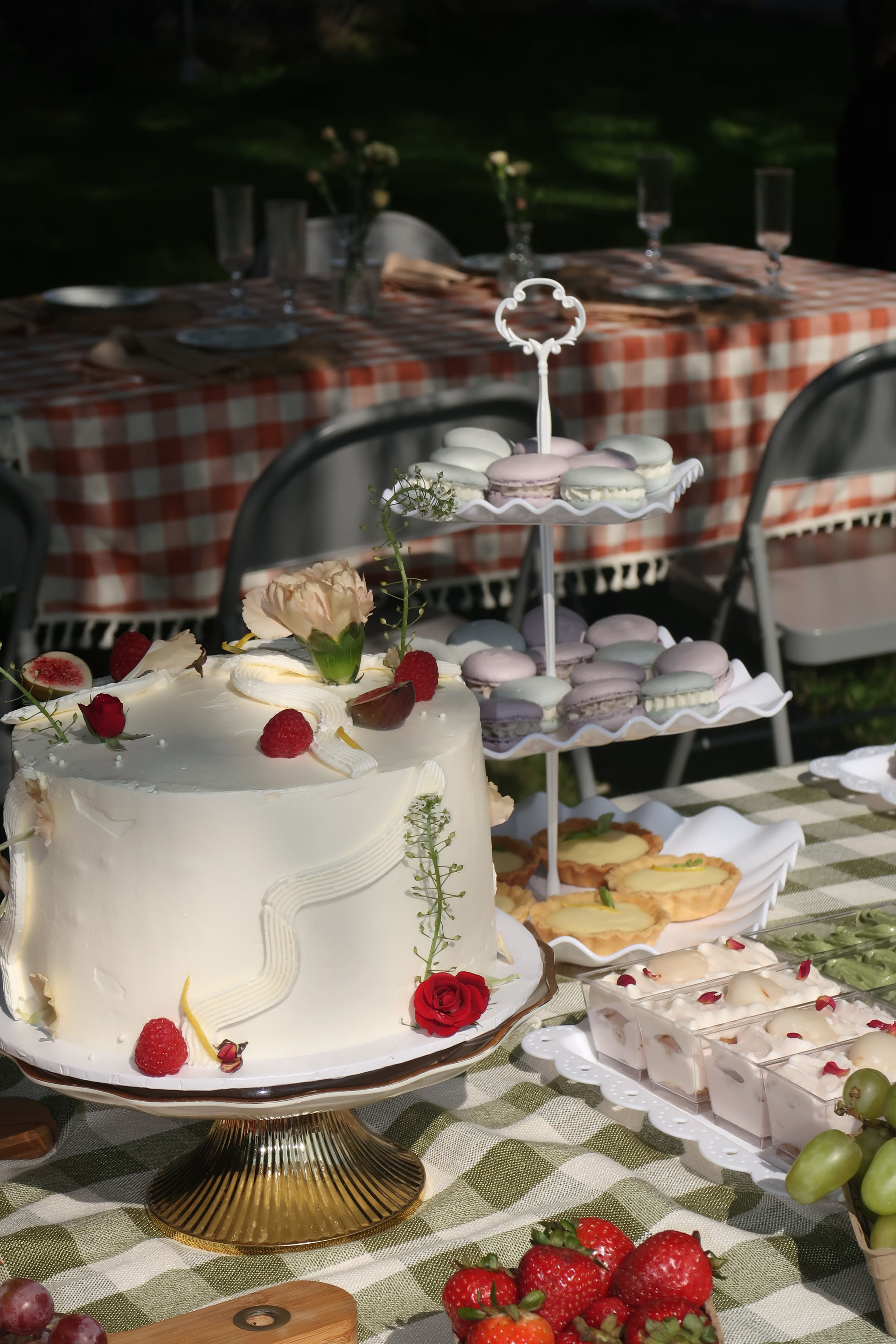 An outdoor table set with cake, pastries and gingham linen