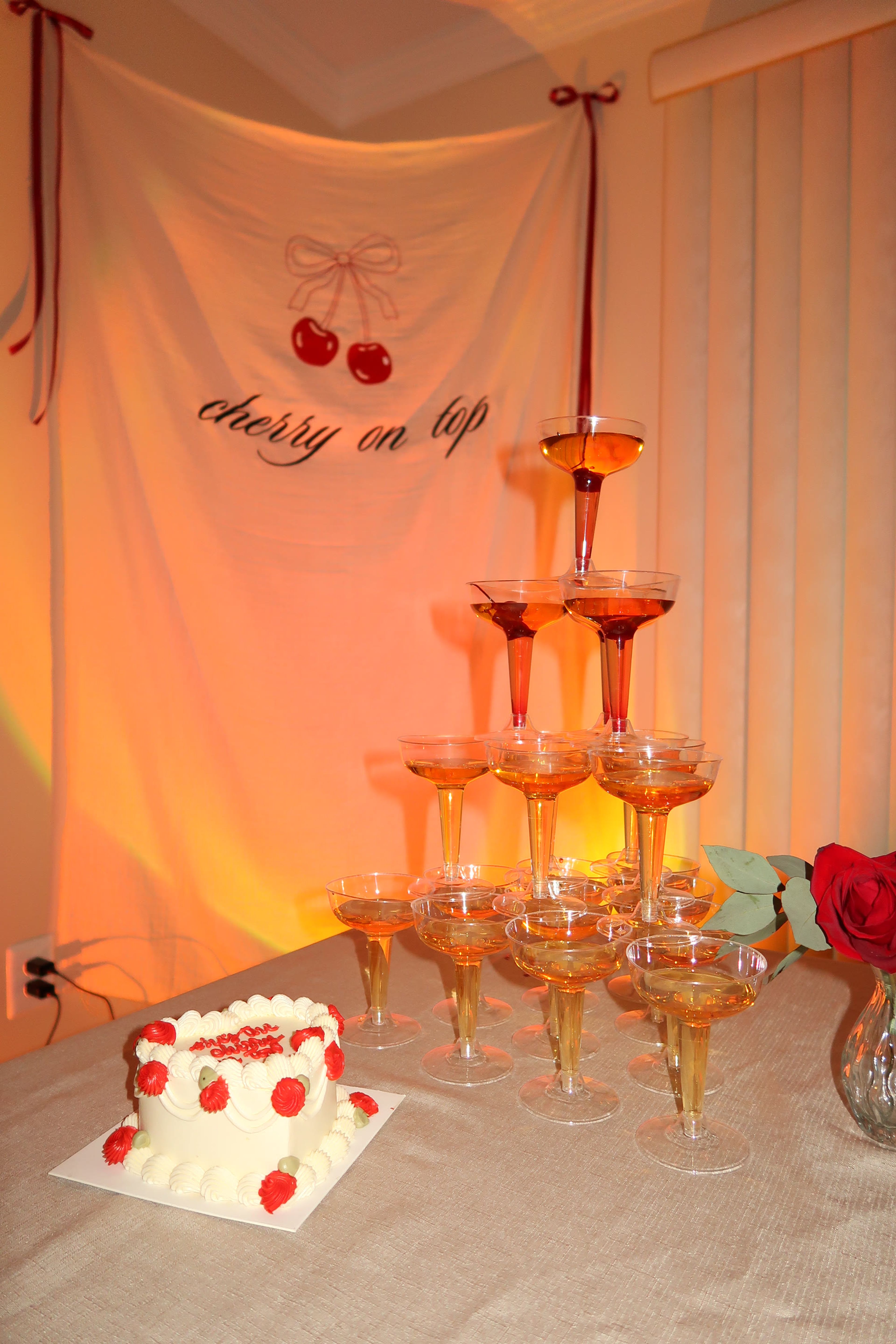 A champagne tower lit warmly with a cake and red roses