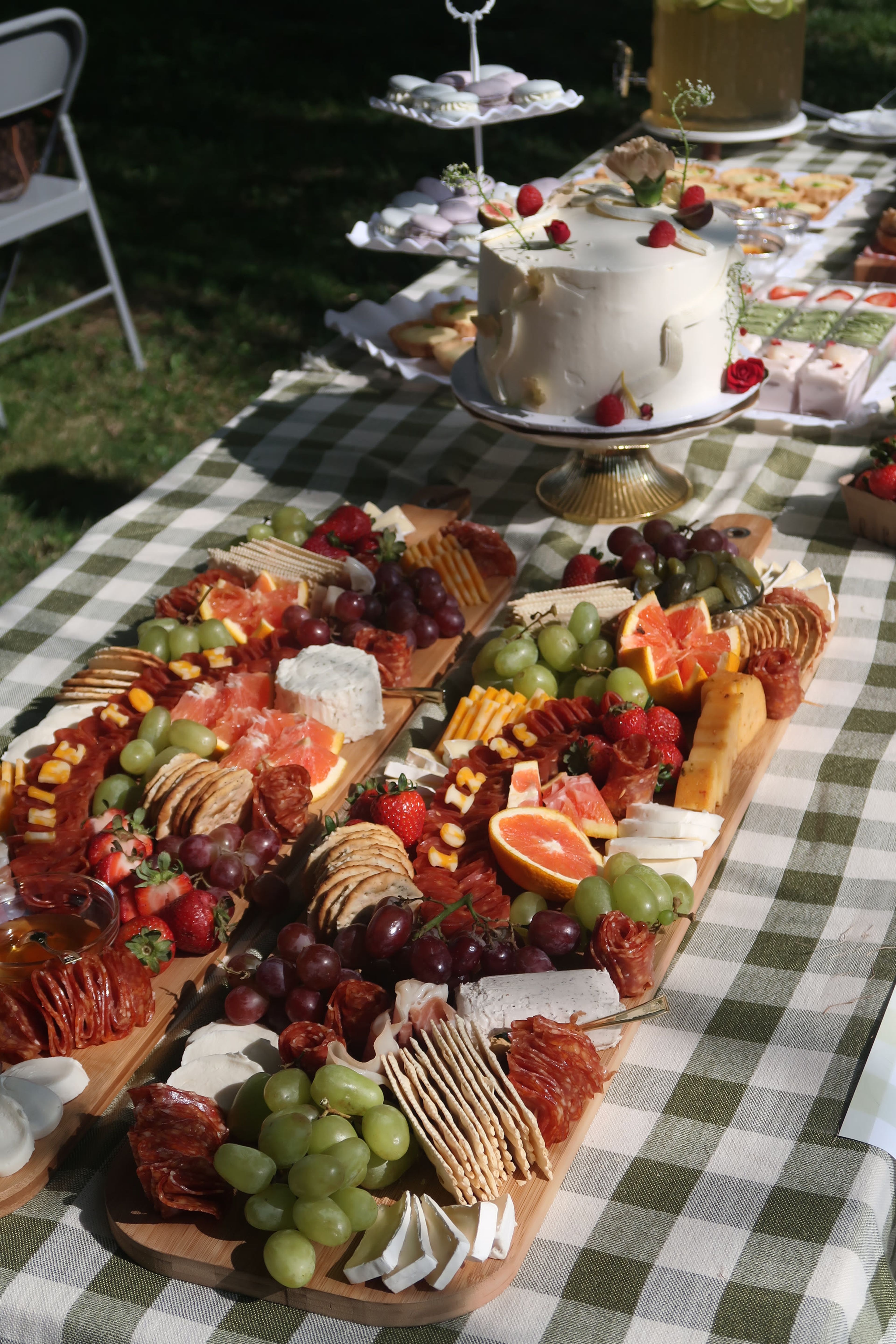 A long grazing table on gingham with a cake stand behind it