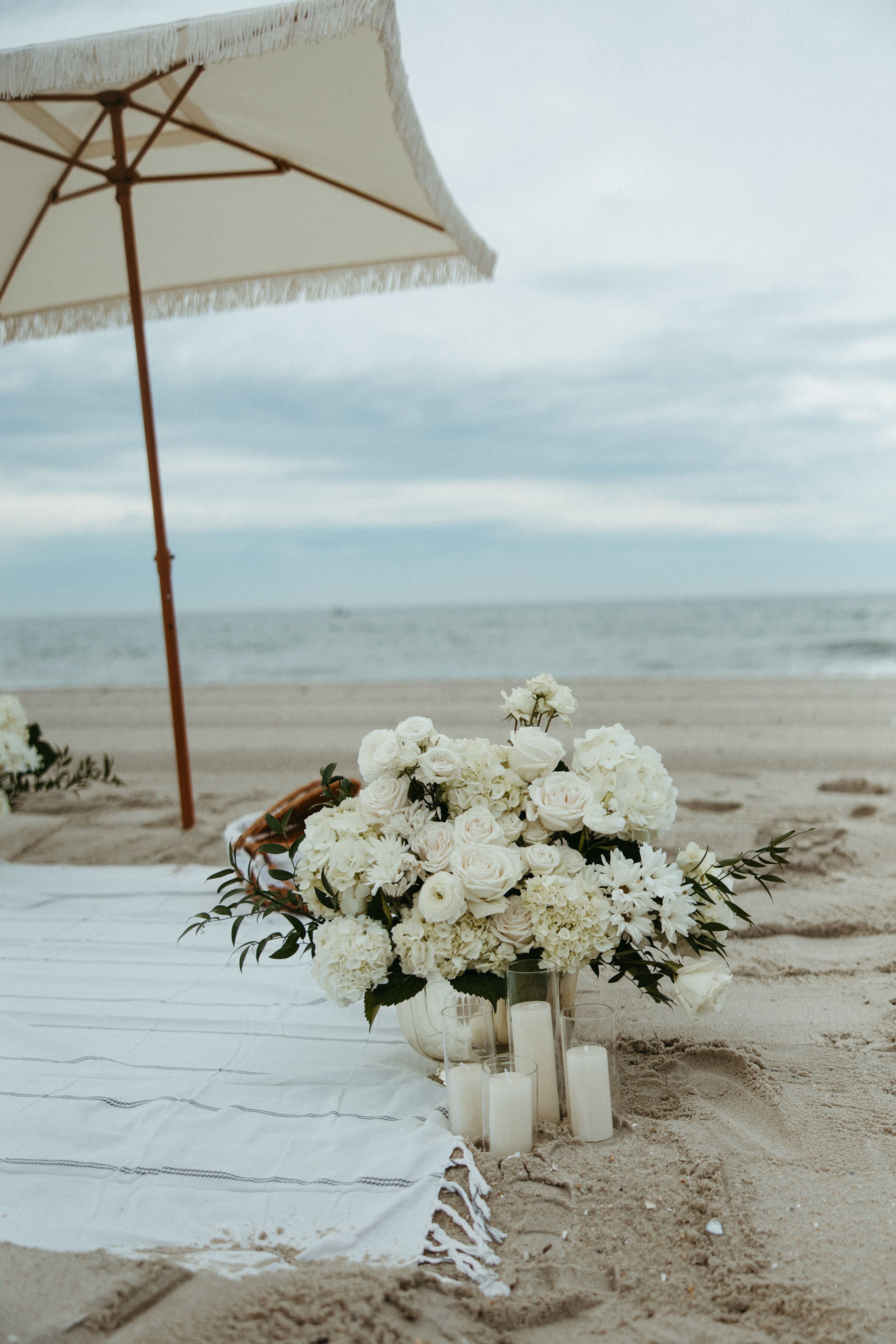 A parasol and floral arrangement on a blanket by the water