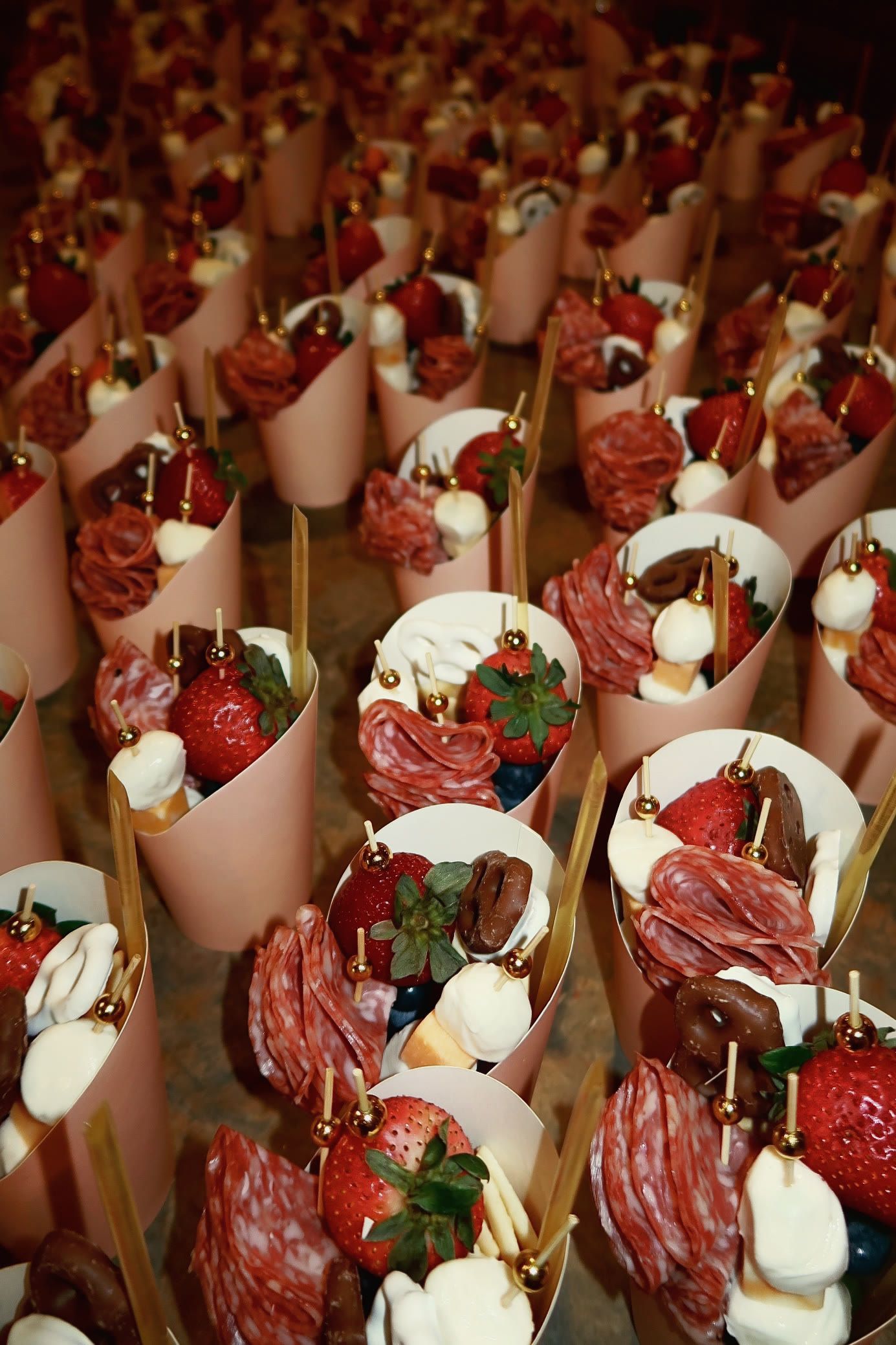 Paper cones of charcuterie topped with strawberries, seen from above