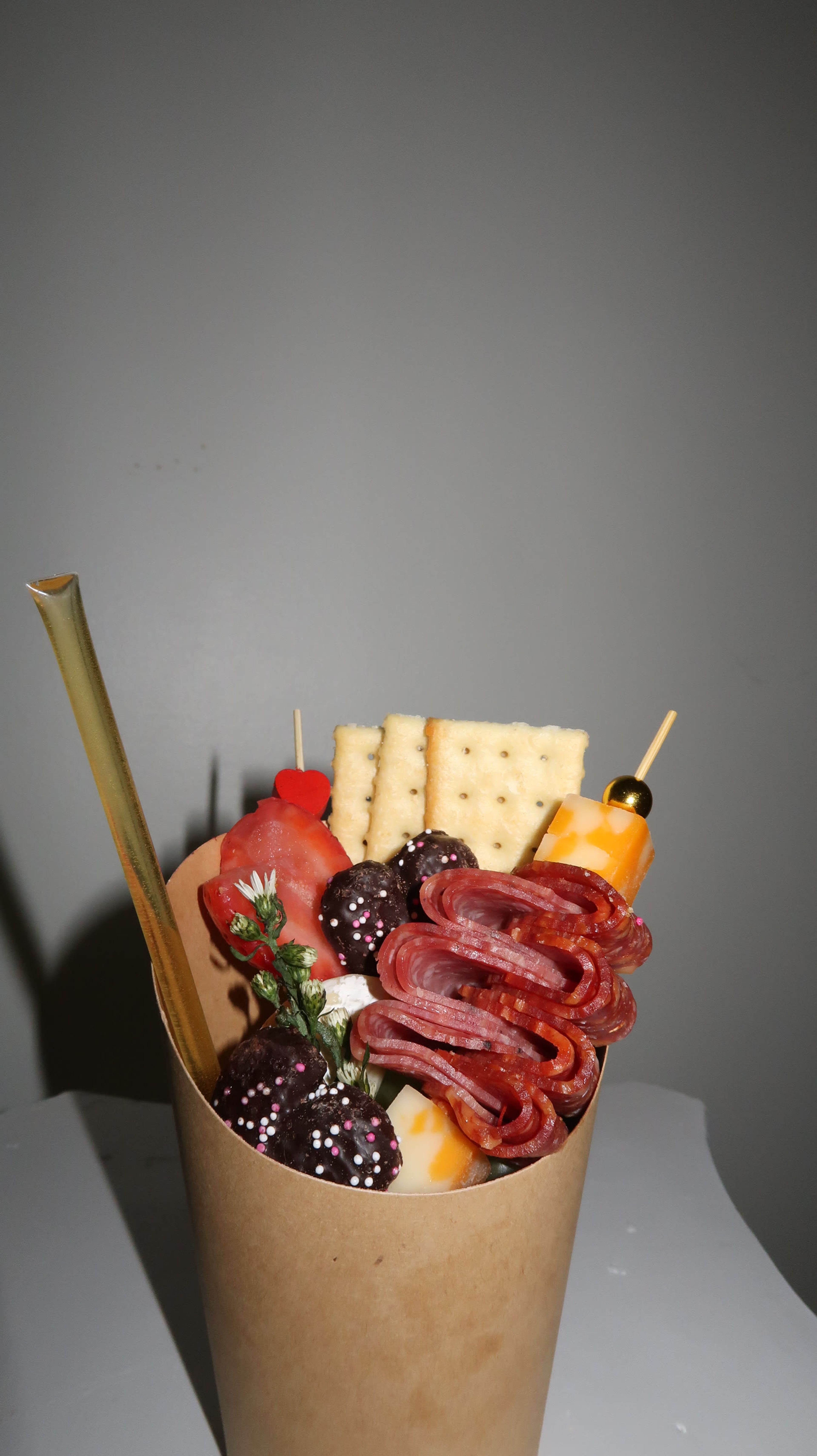 A charcuterie cup of meat and cheese skewers against grey