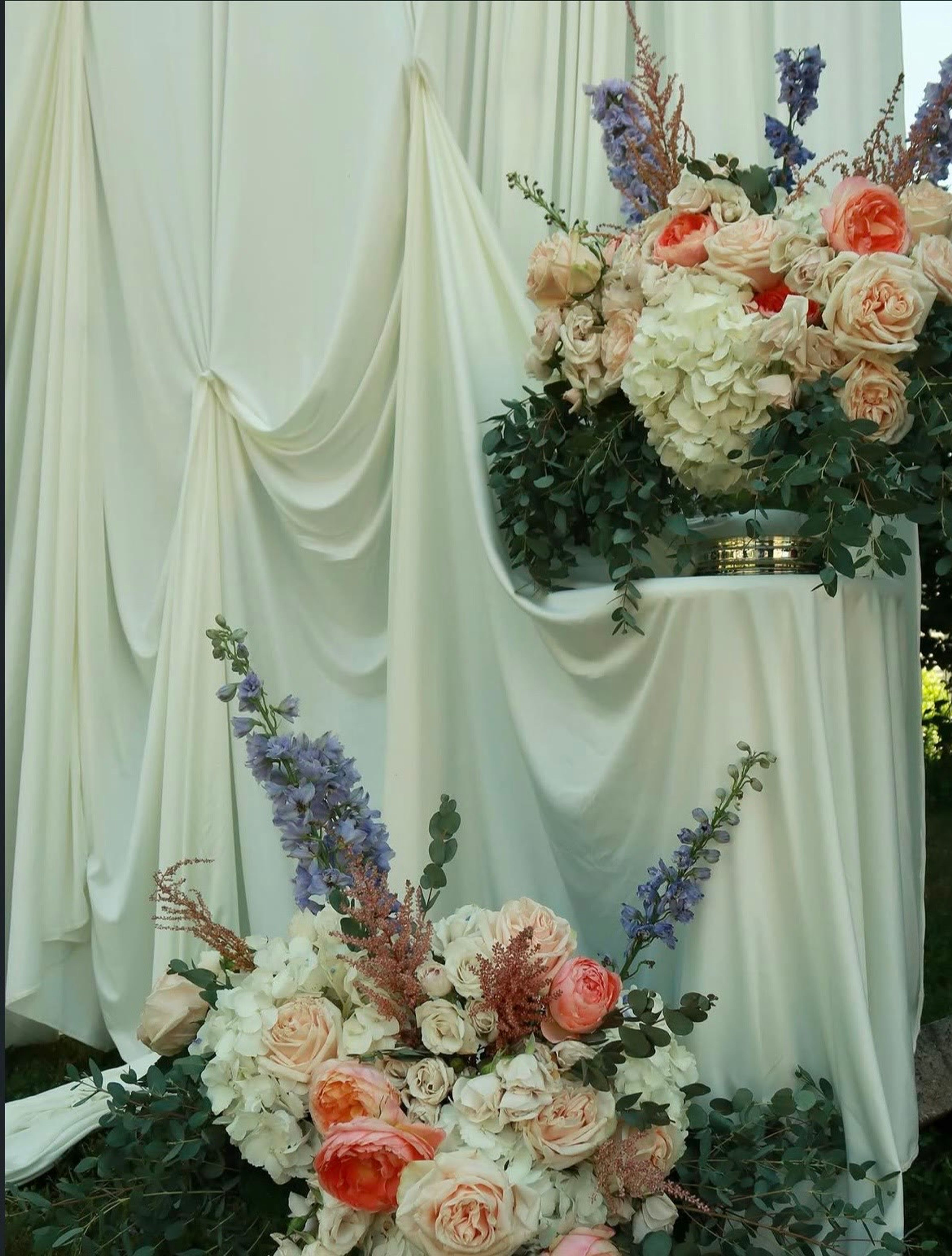 Tall arrangements of roses, hydrangea and larkspur against drapery