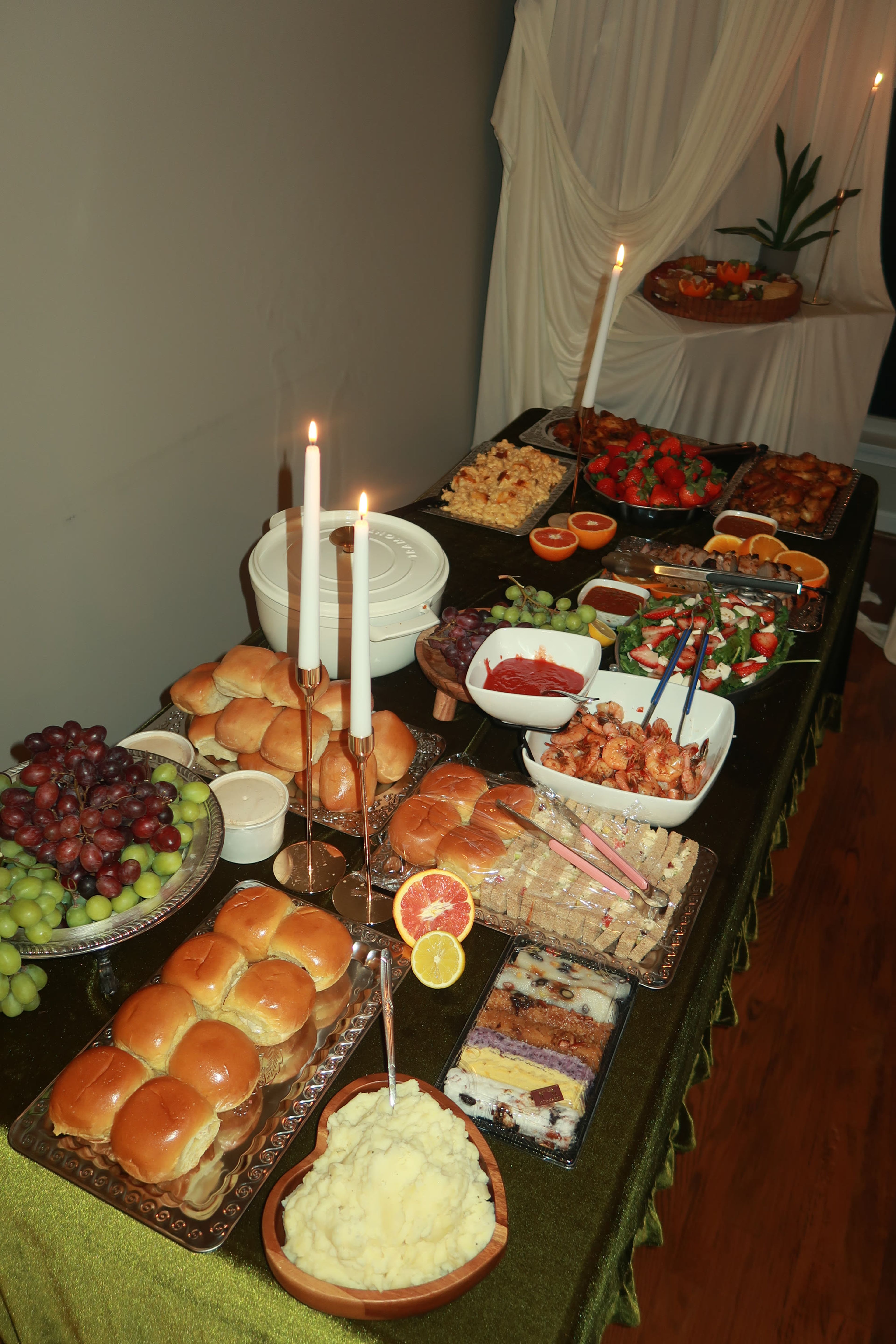 A long candlelit table laid with breads, grapes and platters