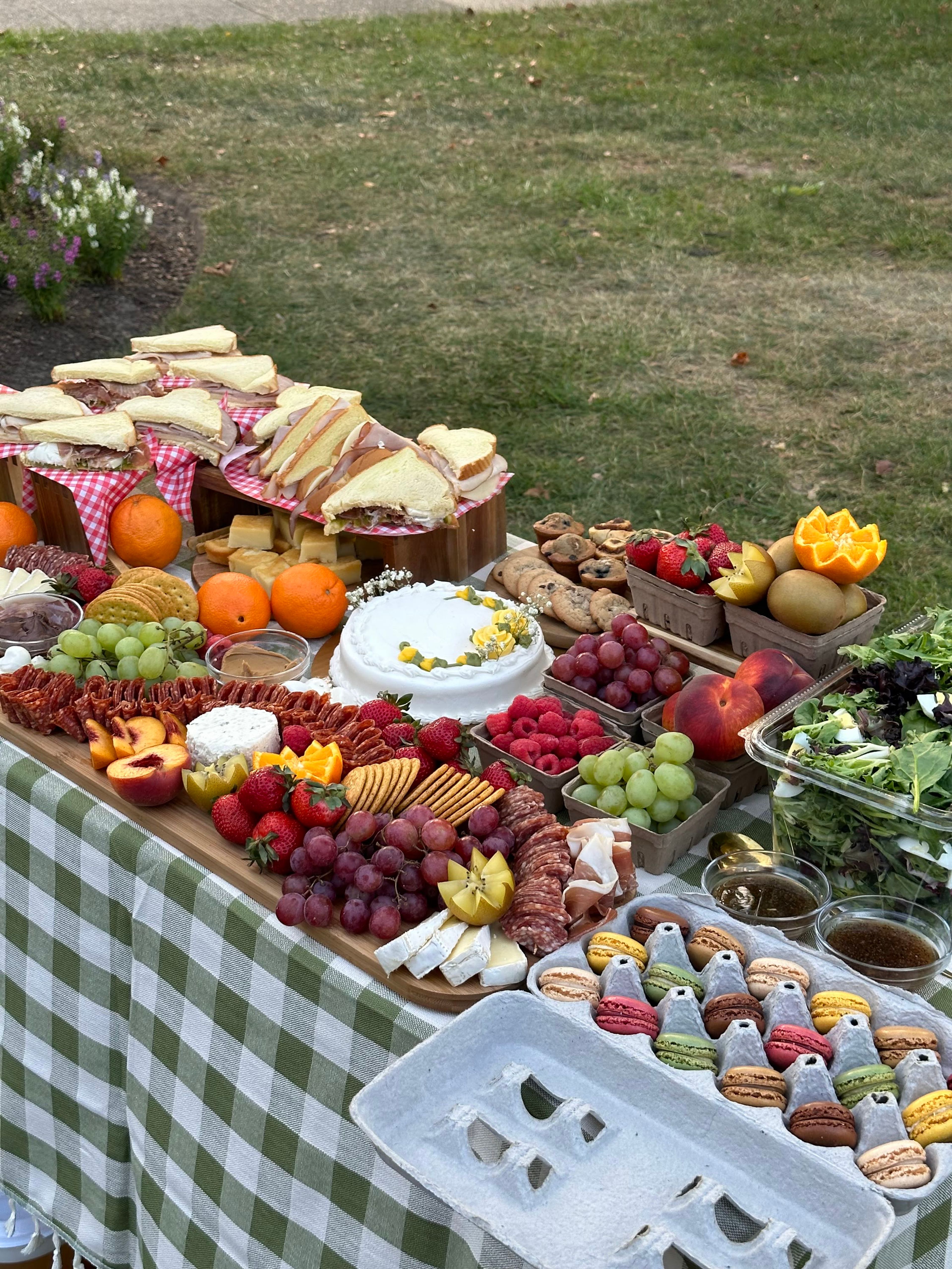 An outdoor buffet of fruit, cupcakes and grazing boards