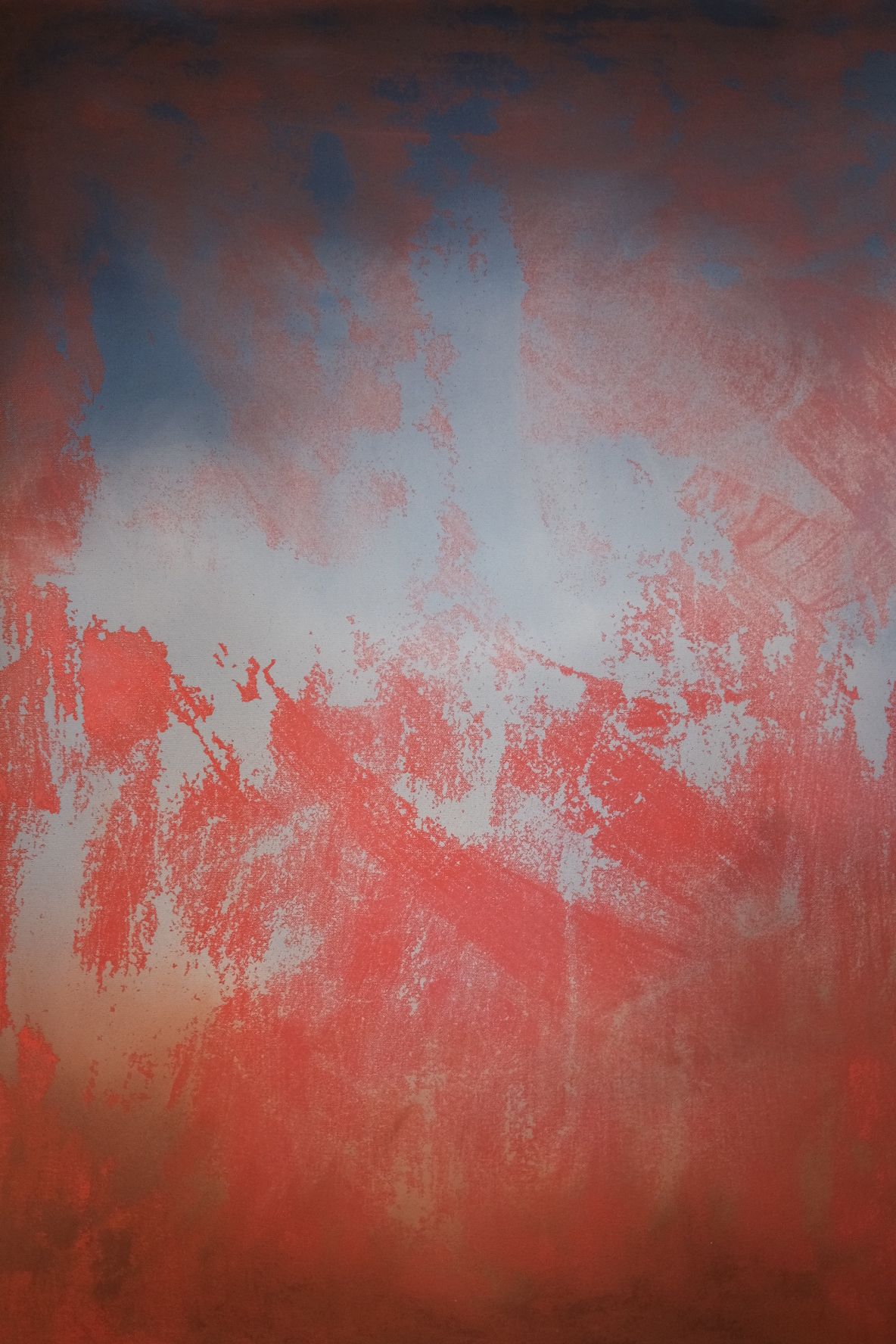 Close up of abstract painting. A deep navy top fades into a hazy pale blue, which is broken up from below by rough, scraped strokes of rust red that take over the lower half.