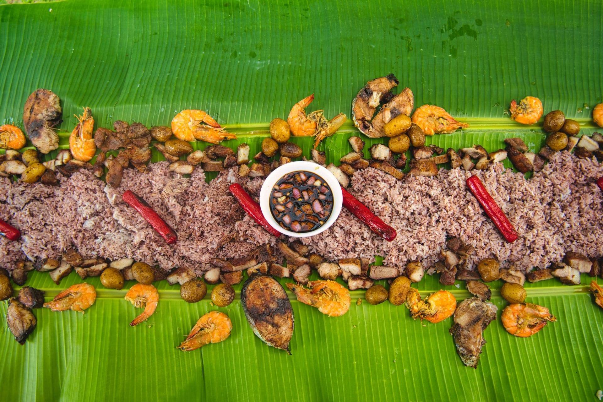 Vibrant boodle fight spread with rice, shrimp and vegetables on banana leaves