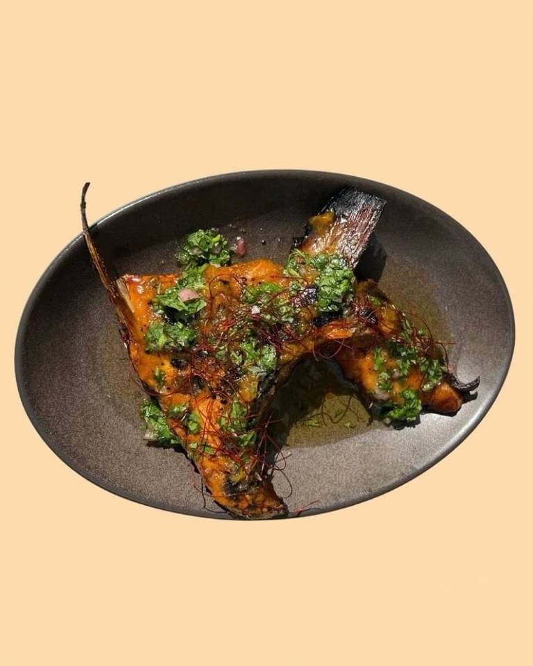 Grilled fish with herb salsa and chilli threads in a dark ceramic bowl, Boodle Fight Stirchley