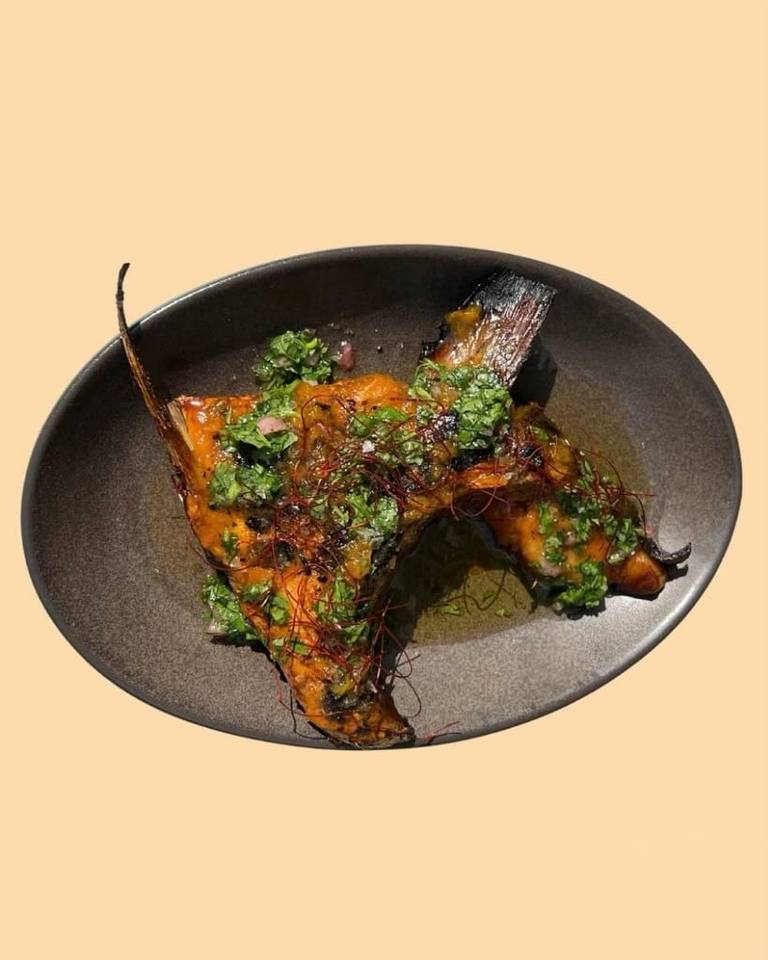 Grilled fish with herb salsa and chilli threads in a dark ceramic bowl, Boodle Fight Stirchley