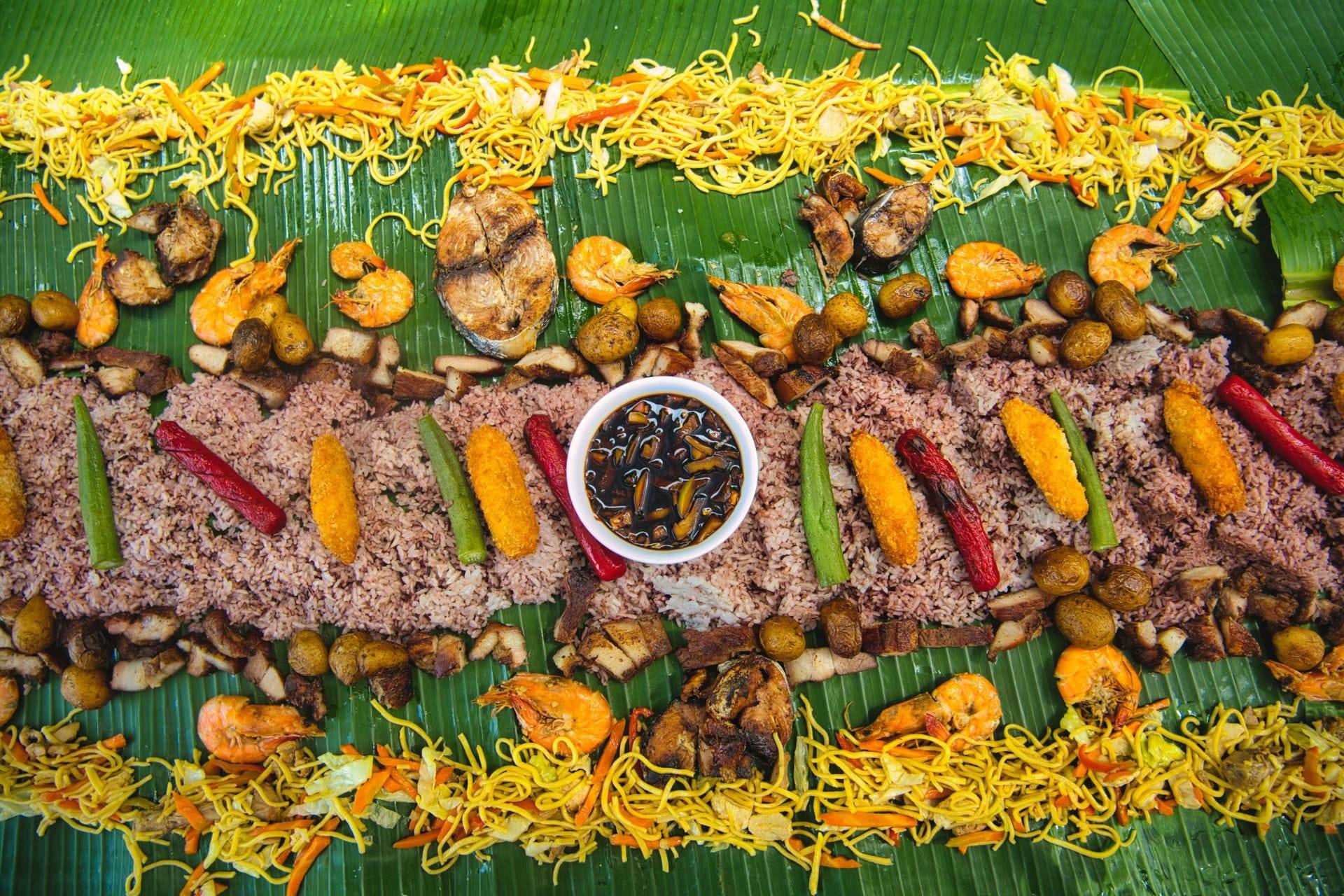 Filipino boodle fight with rice, seafood and vegetables on banana leaves