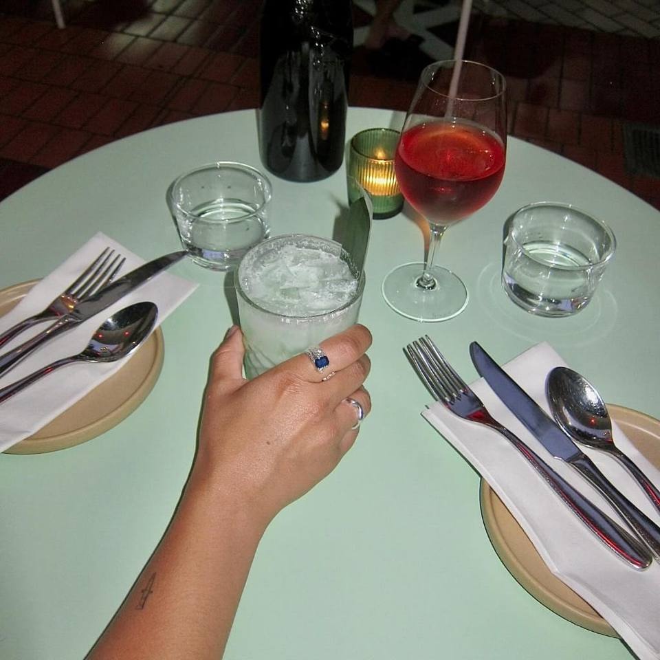 Hand reaching for a cocktail at a candlelit mint-green table set for two, Boodle Fight Stirchley