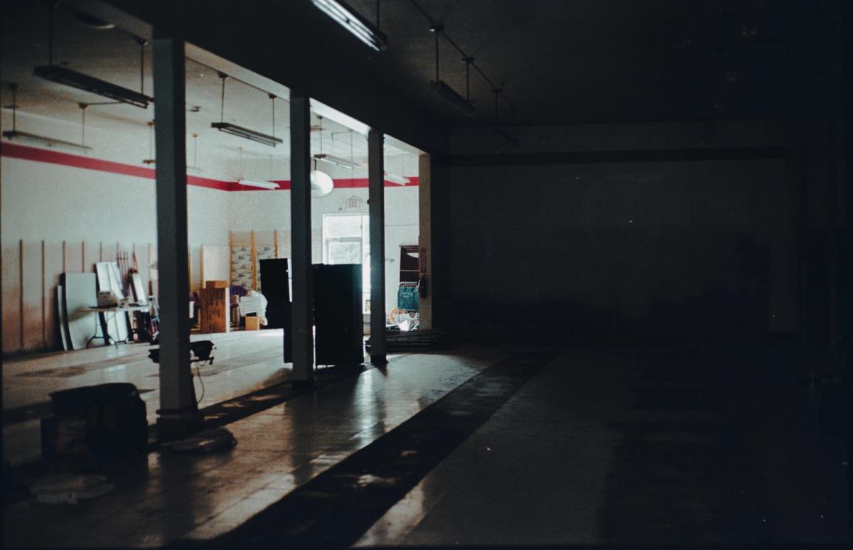 An empty storefront interior, pillars and stacked fixtures in the light from the windows.