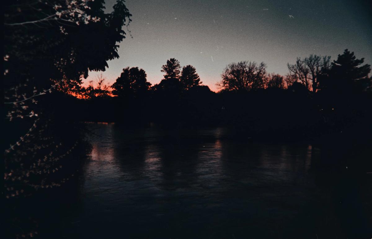 A river at dusk, dark trees silhouetted against a last orange glow.