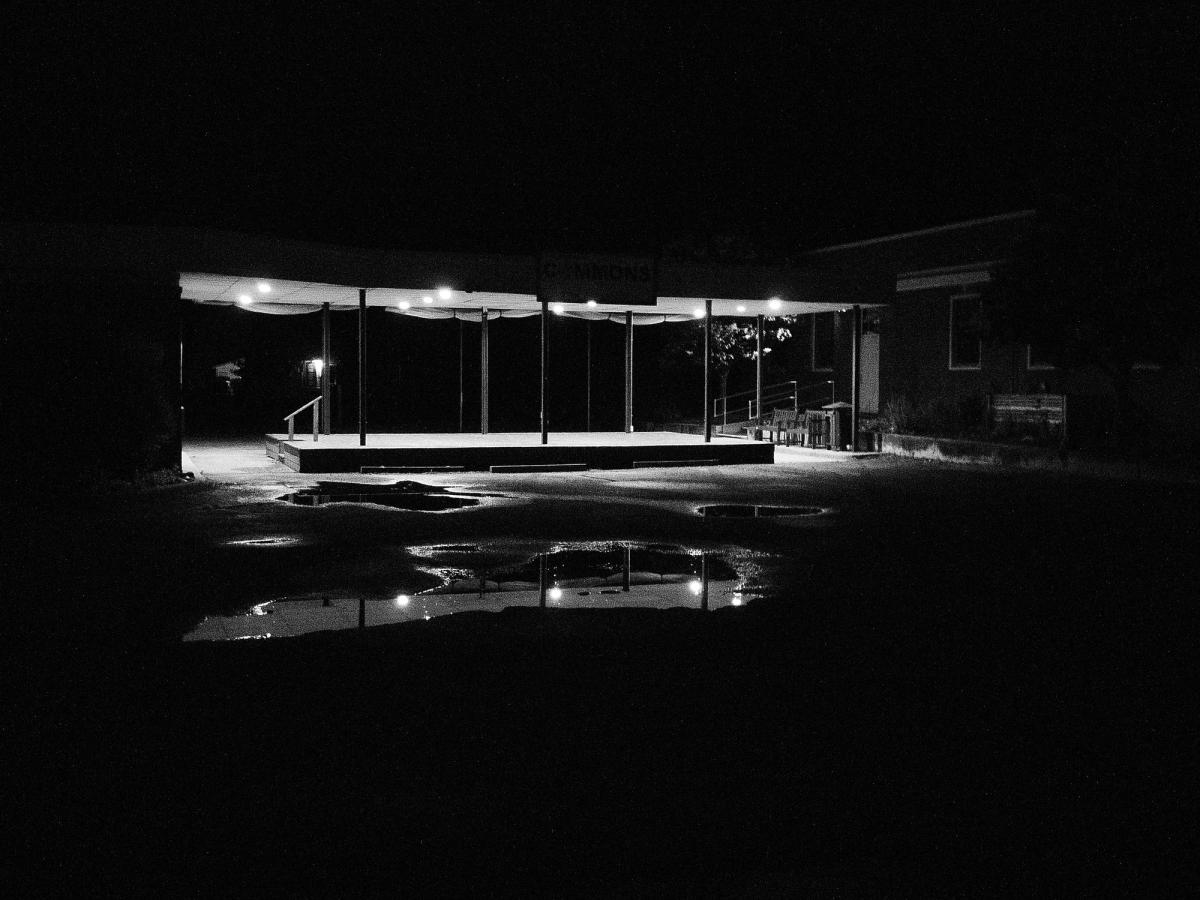 An empty lit pavilion at night, its lights reflected in puddles across the lot.