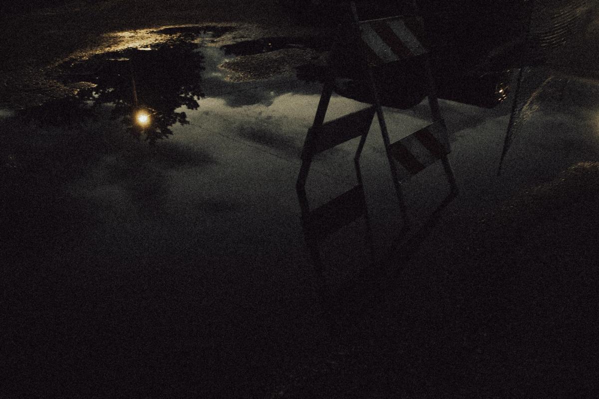 A striped barricade and a streetlamp mirrored in a night puddle.