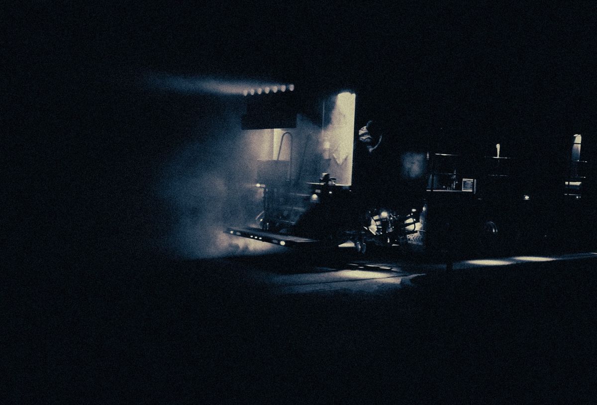 A spray truck working at night, its dust lit by a bar of white light.