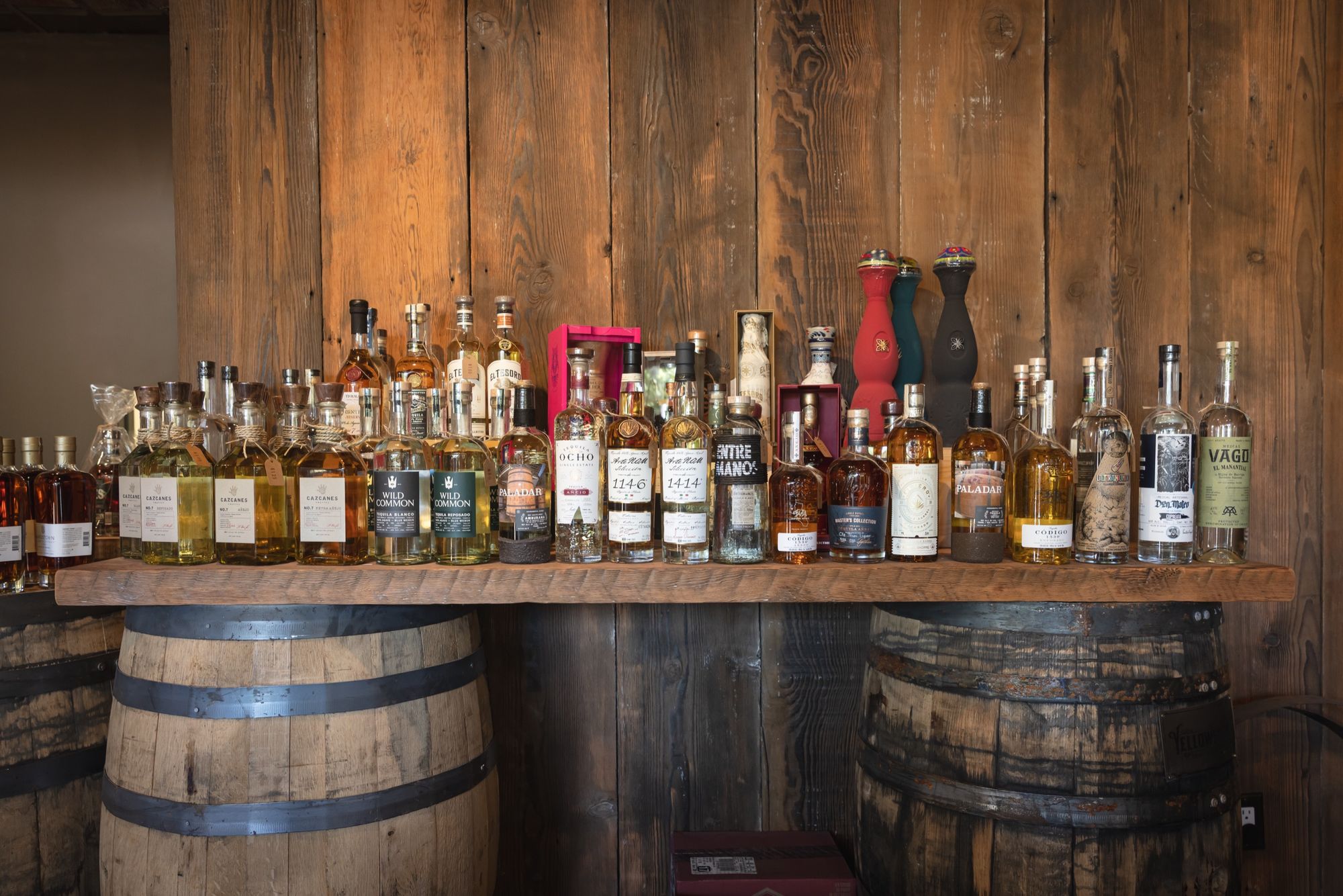 Agave bottles lined along a reclaimed-wood shelf set on whiskey barrels at Barrel Shoppe
