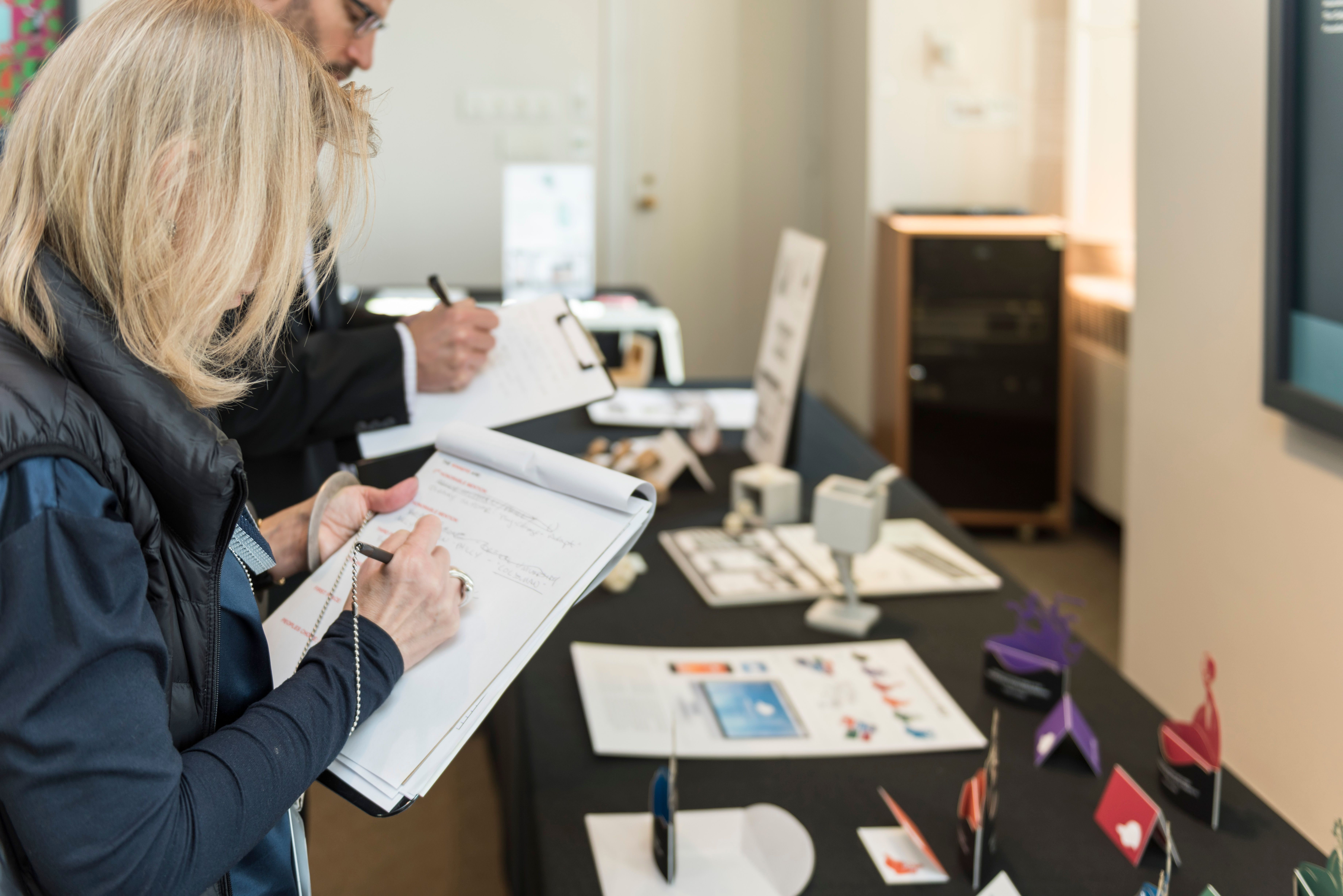 A judge taking notes on a clipboard while looking at design projects