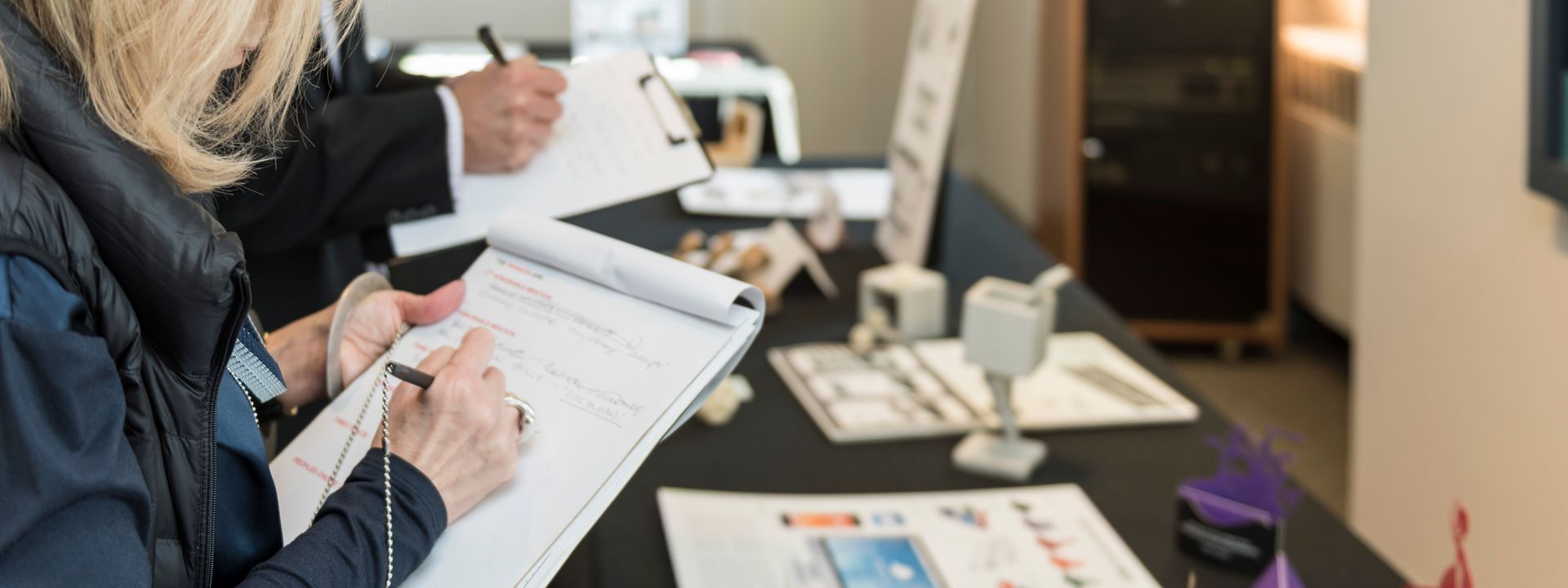 A judge taking notes on a clipboard while looking at design projects