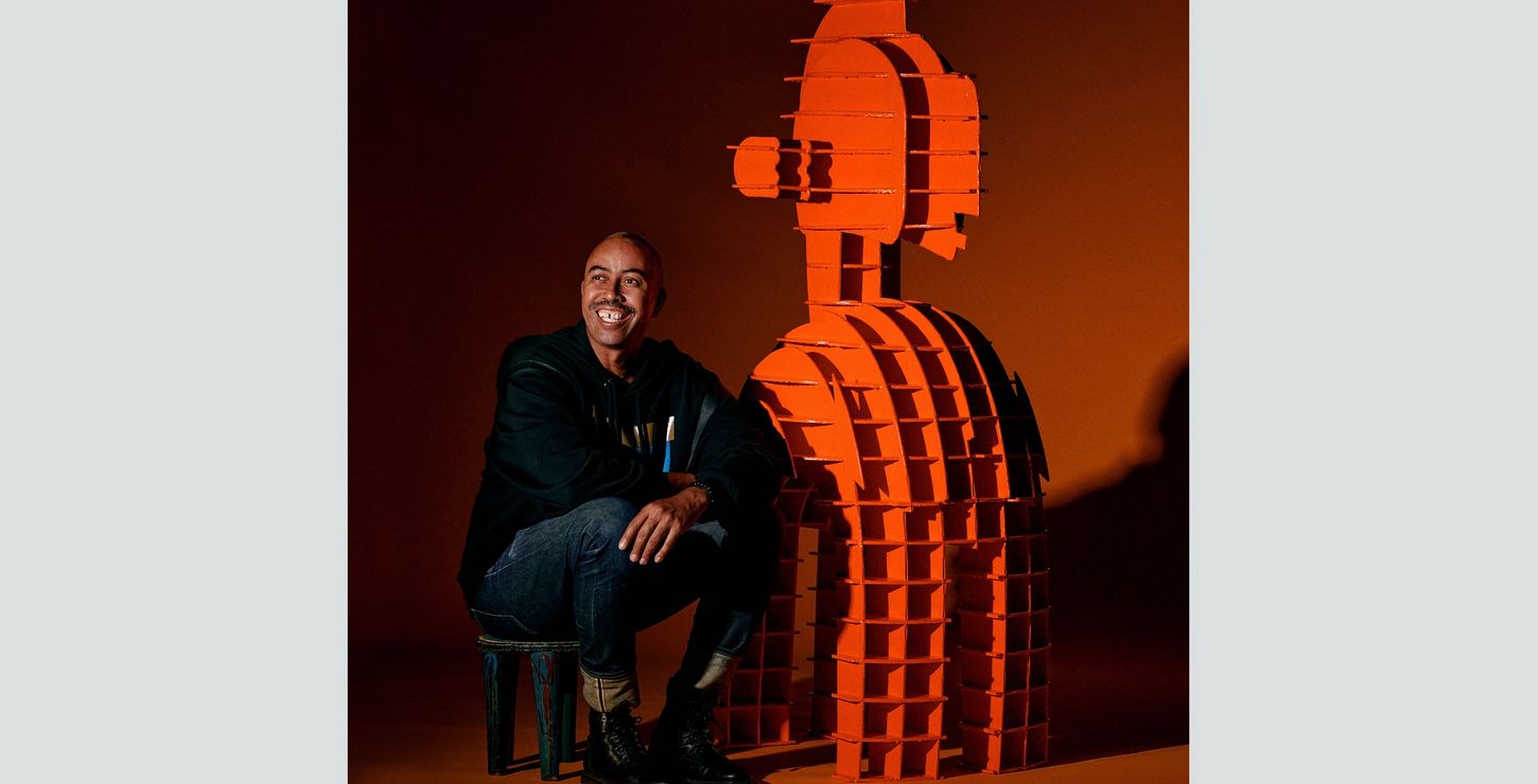 A photograph of Stephen Burks sitting next to his sculpture.