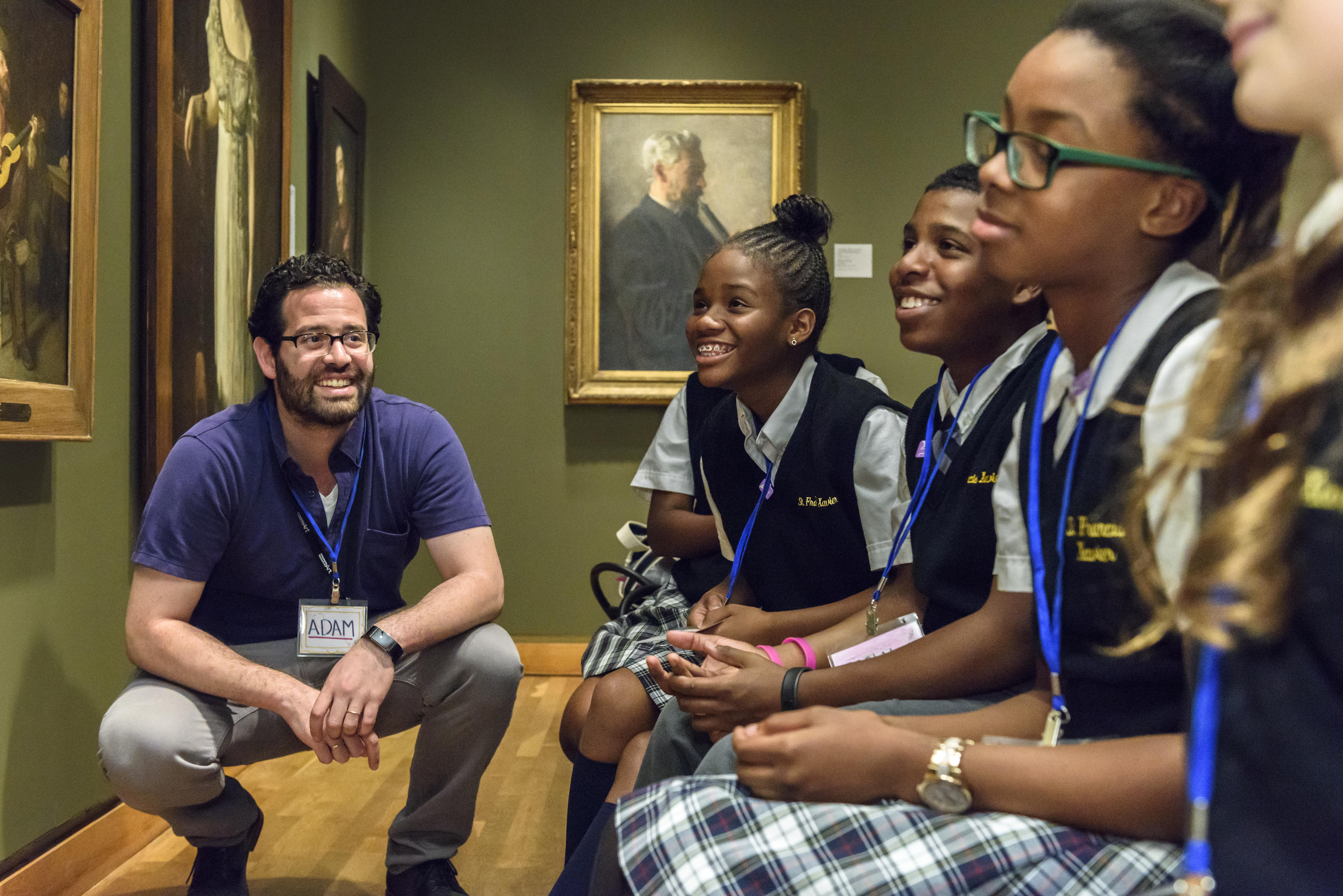 Teacher and students smiling together while looking at artwork in a gallery