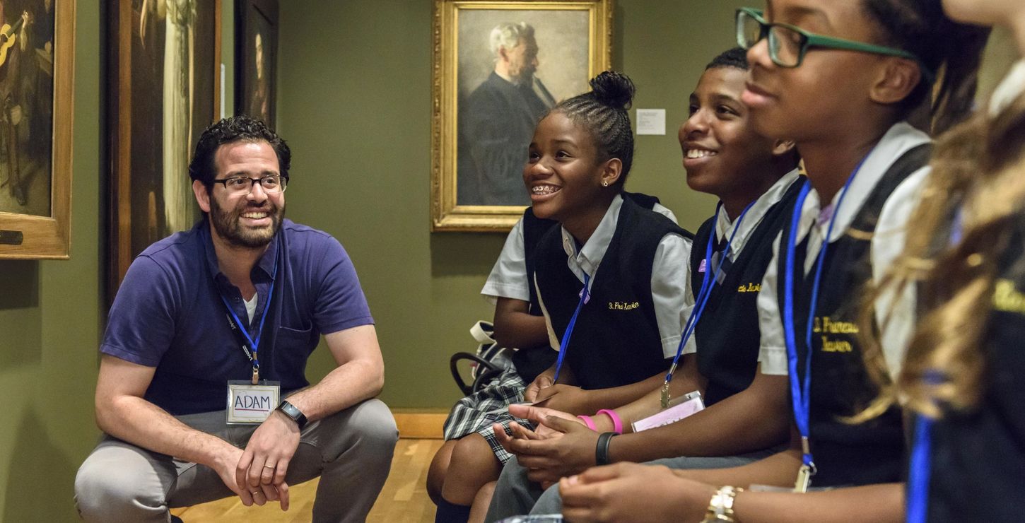 Teacher and students smiling together while looking at artwork in a gallery