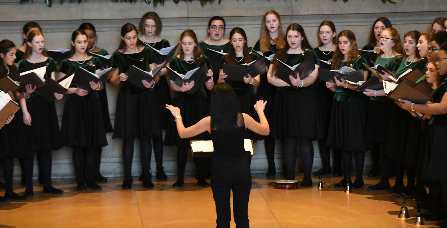 An all girl choir being directed through a song.