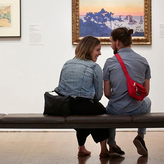 A young couple chat while seated on a bench in a gallery