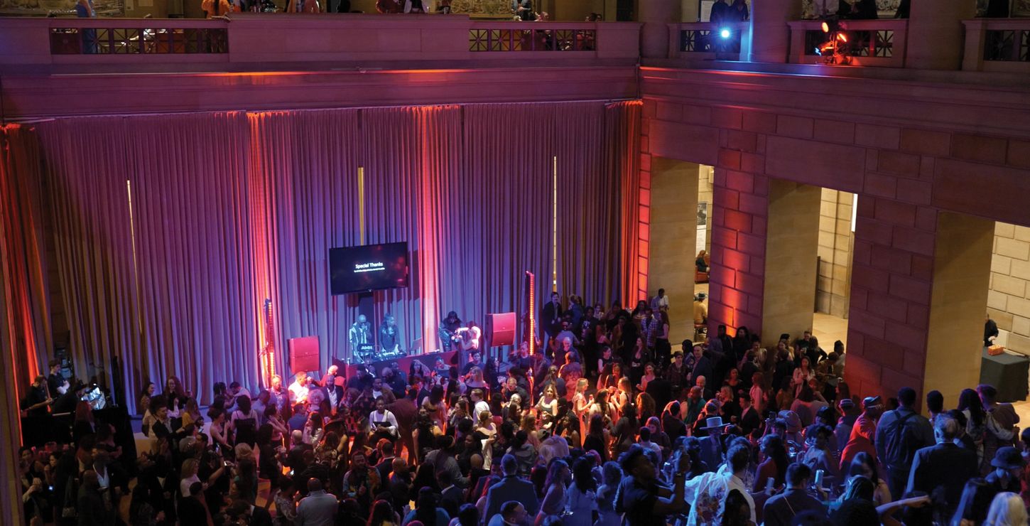 Art-ish 2024 Key Image. Crowd of people dancing in the Great Stair Hall surrounded by pink and purple lights.