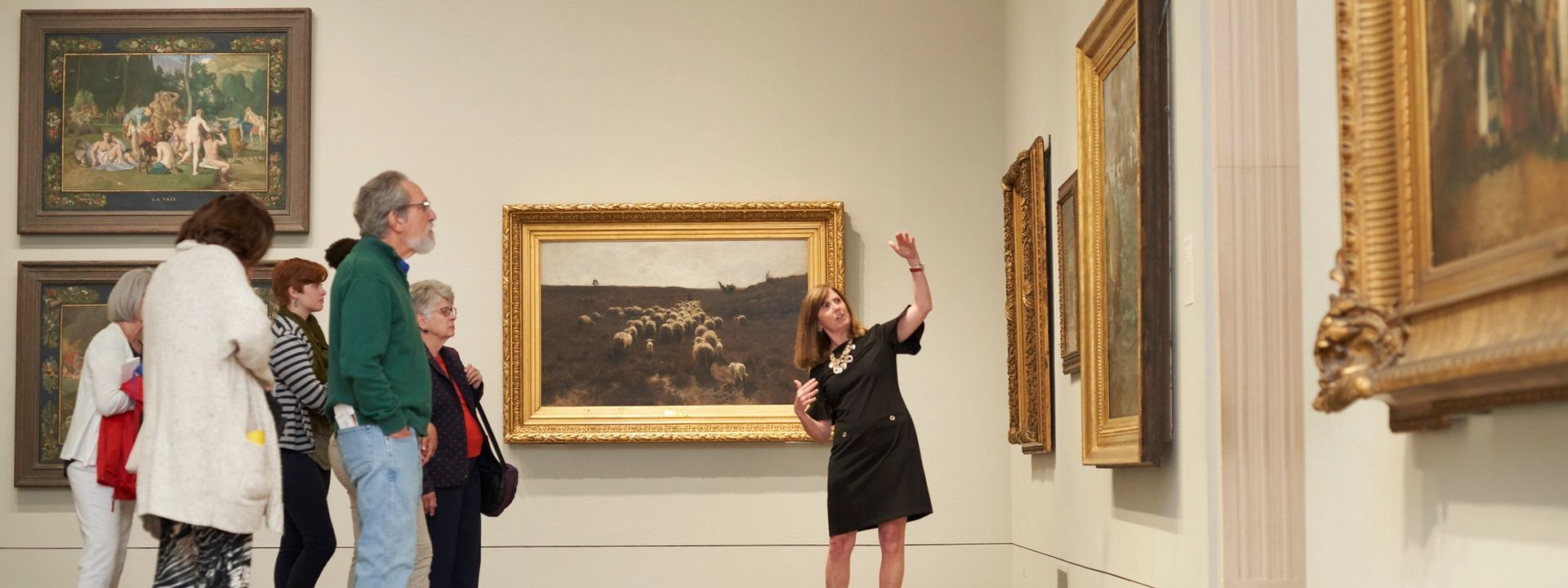 A museum guide leading a tour group and pointing up to a painting