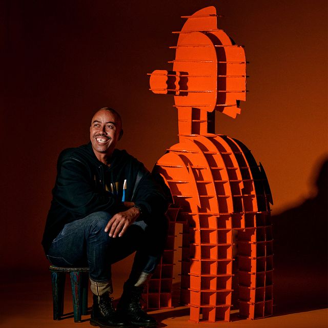 Photograph of artist Stephen Burks sitting next to one of his sculptures.