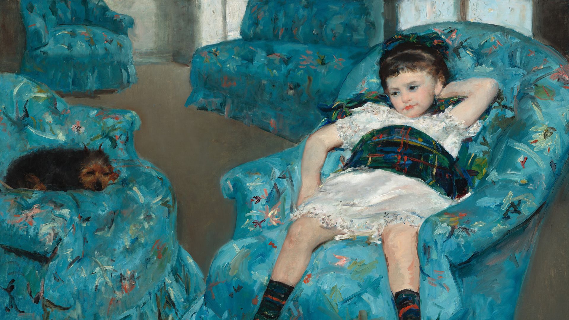 A little girl is sitting in a blue chair with a dog opposite her.