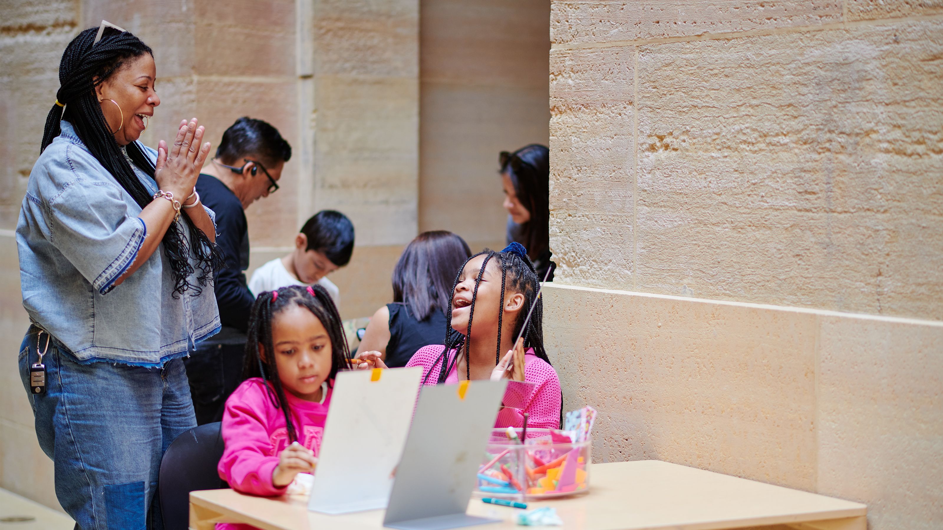 Photo of one woman and two girls participating in art activities in the foreground.
