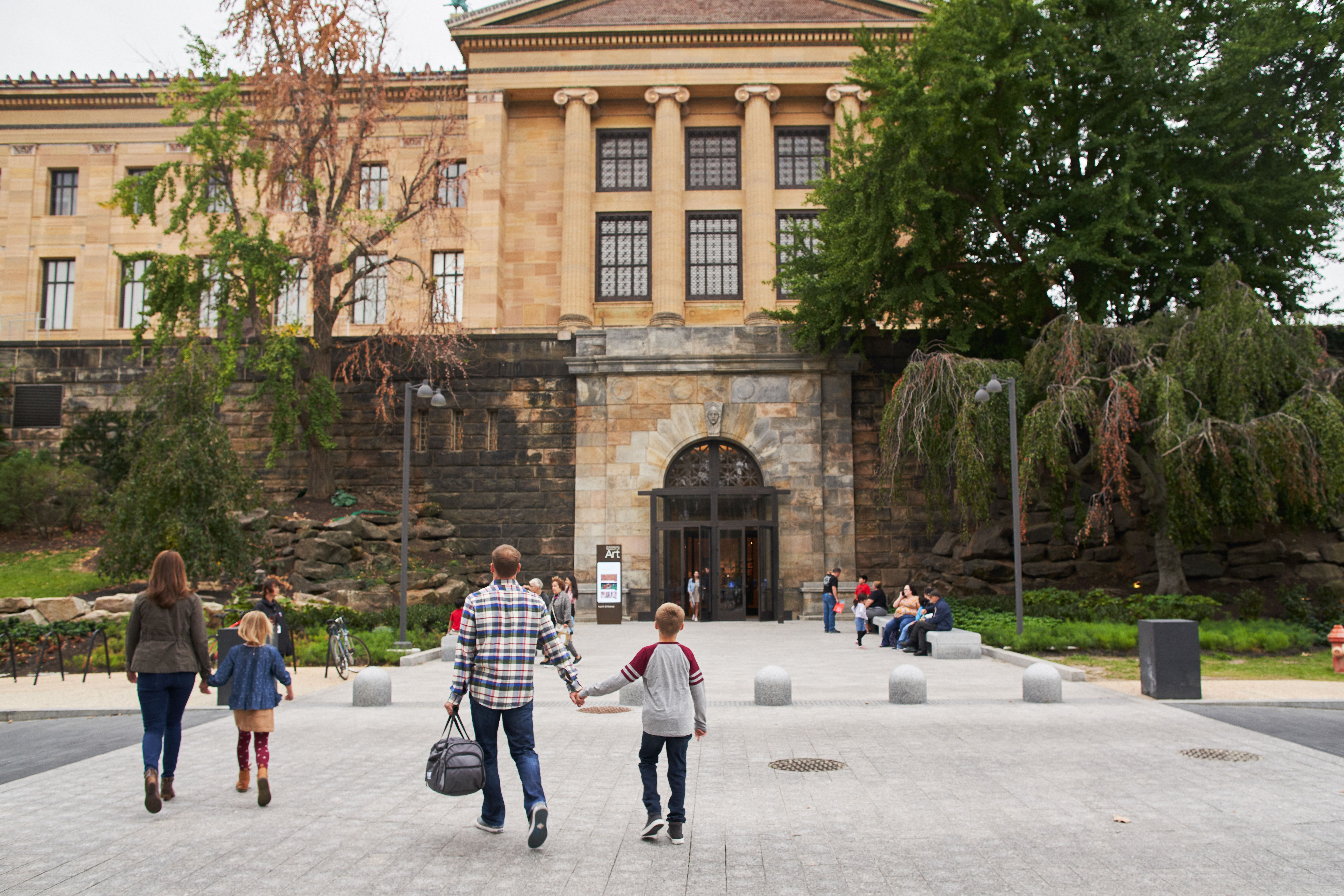 An adult and child holding hands walking up to the museum