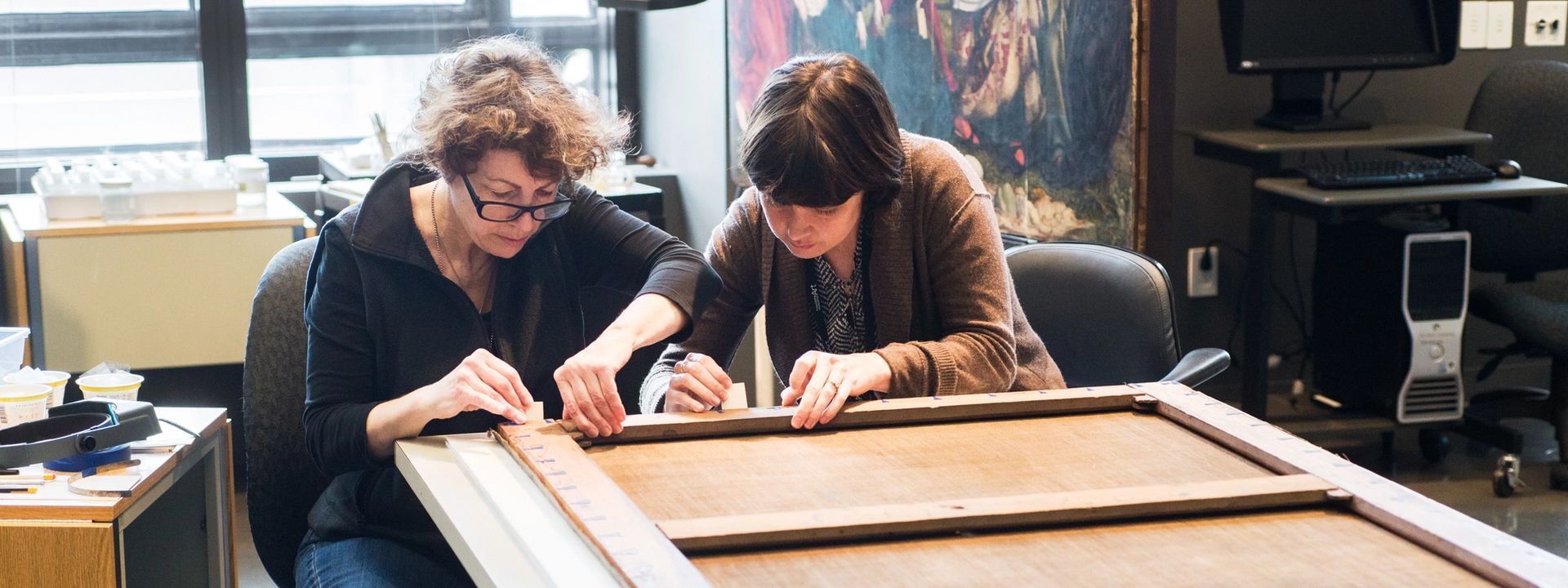 Two conservators working on a framed artwork