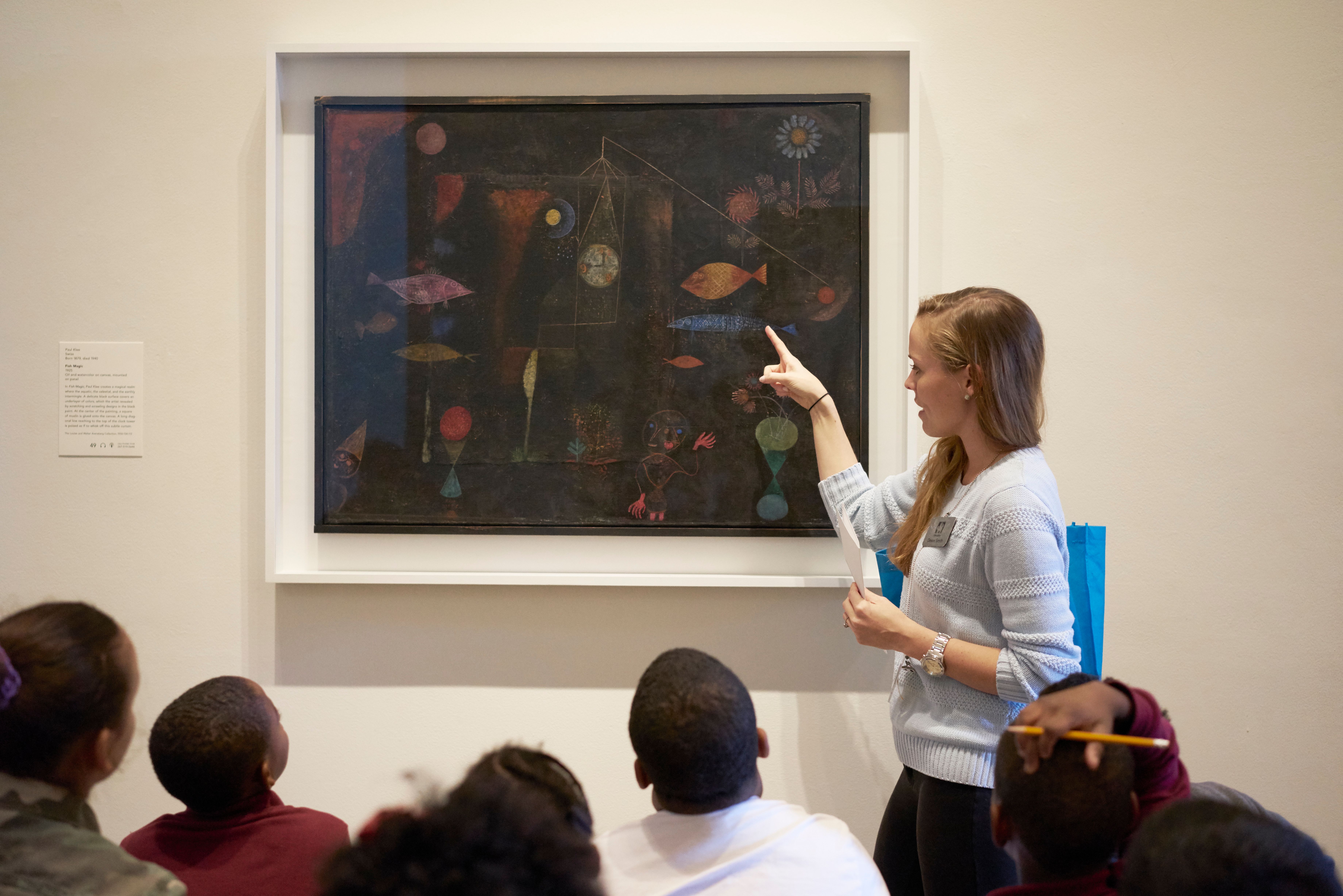 Teacher pointing to an artwork in a gallery and leading a student workshop