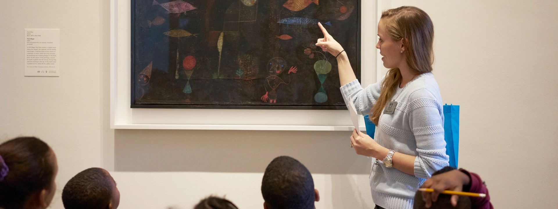 Teacher pointing to an artwork in a gallery and leading a student workshop
