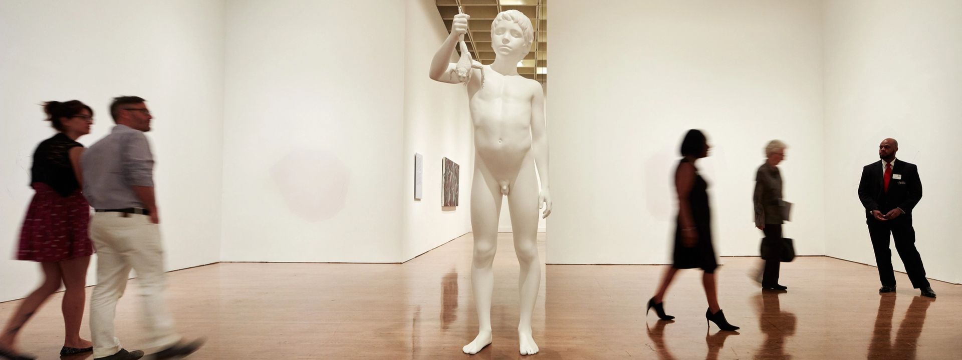 People walking around a large statue in a gallery