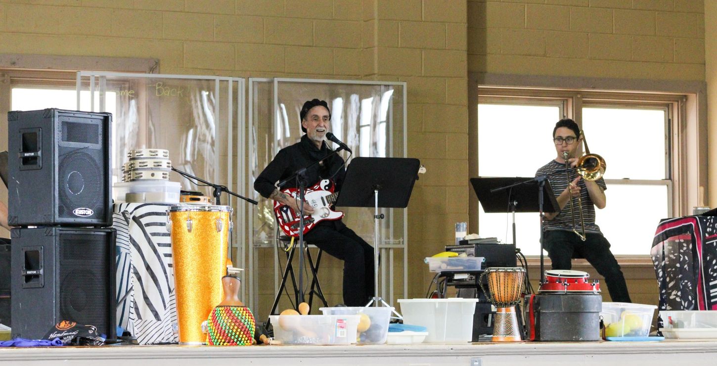 Two Latino musicians, one playing an electric guitar and the other playing a trombone.
