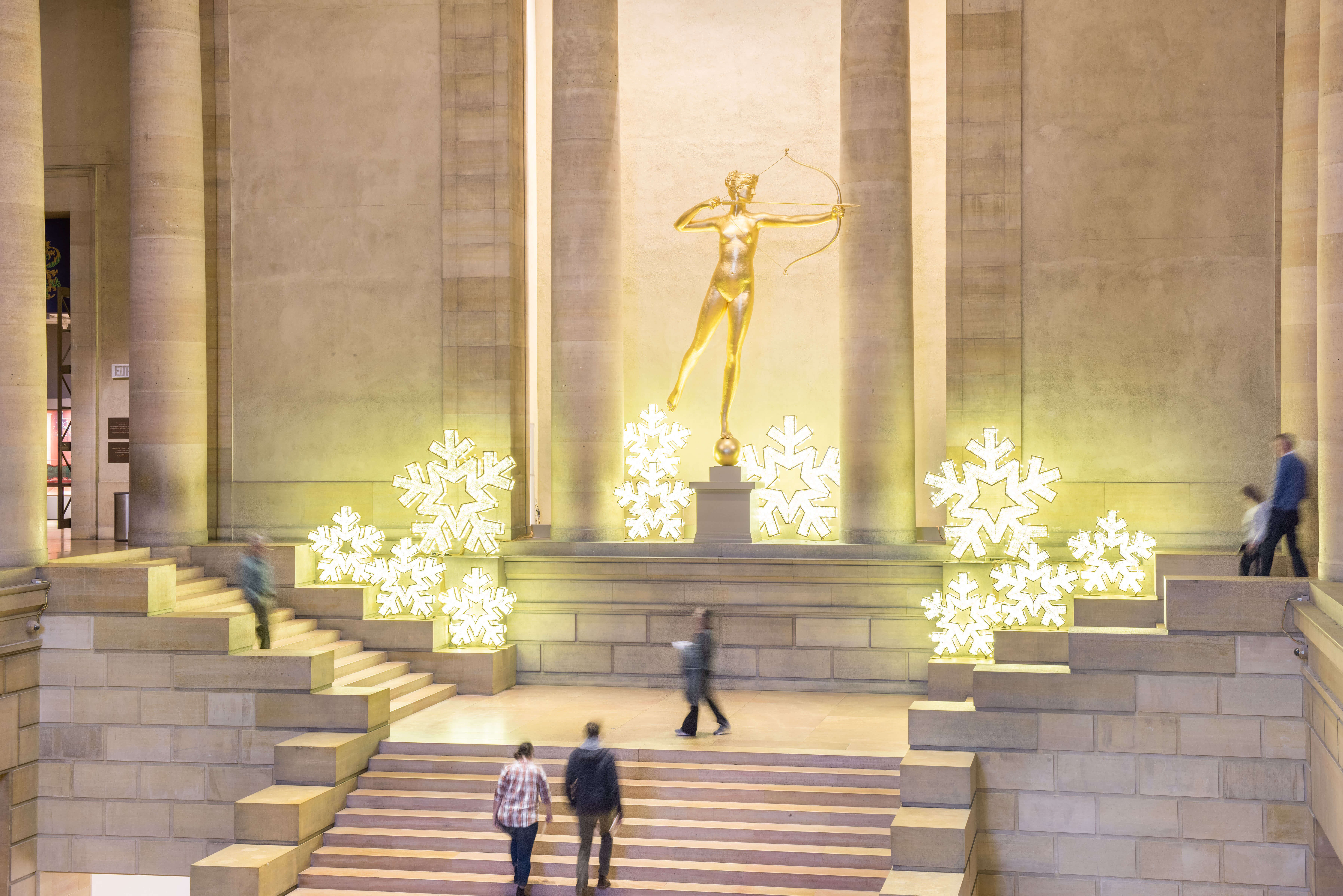 Gilded Diana sculpture surrounded by large, lit up snowflake decorations in the Great Stair Hall