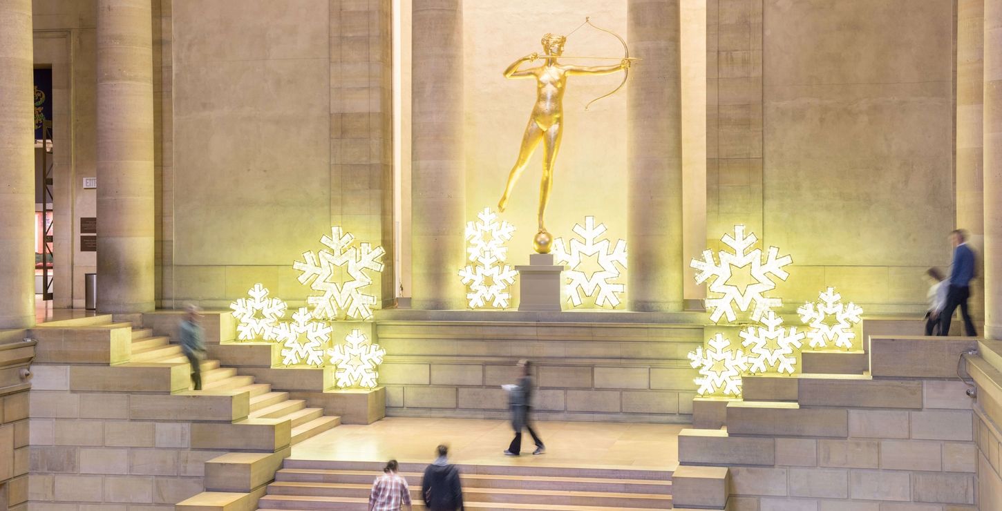 Gilded Diana sculpture surrounded by large, lit up snowflake decorations in the Great Stair Hall